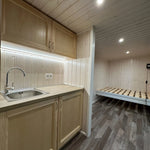 The Large GlampTainer container-style glamping unit – light timber kitchenette with LED strip lighting opposite built-in wooden bed frame