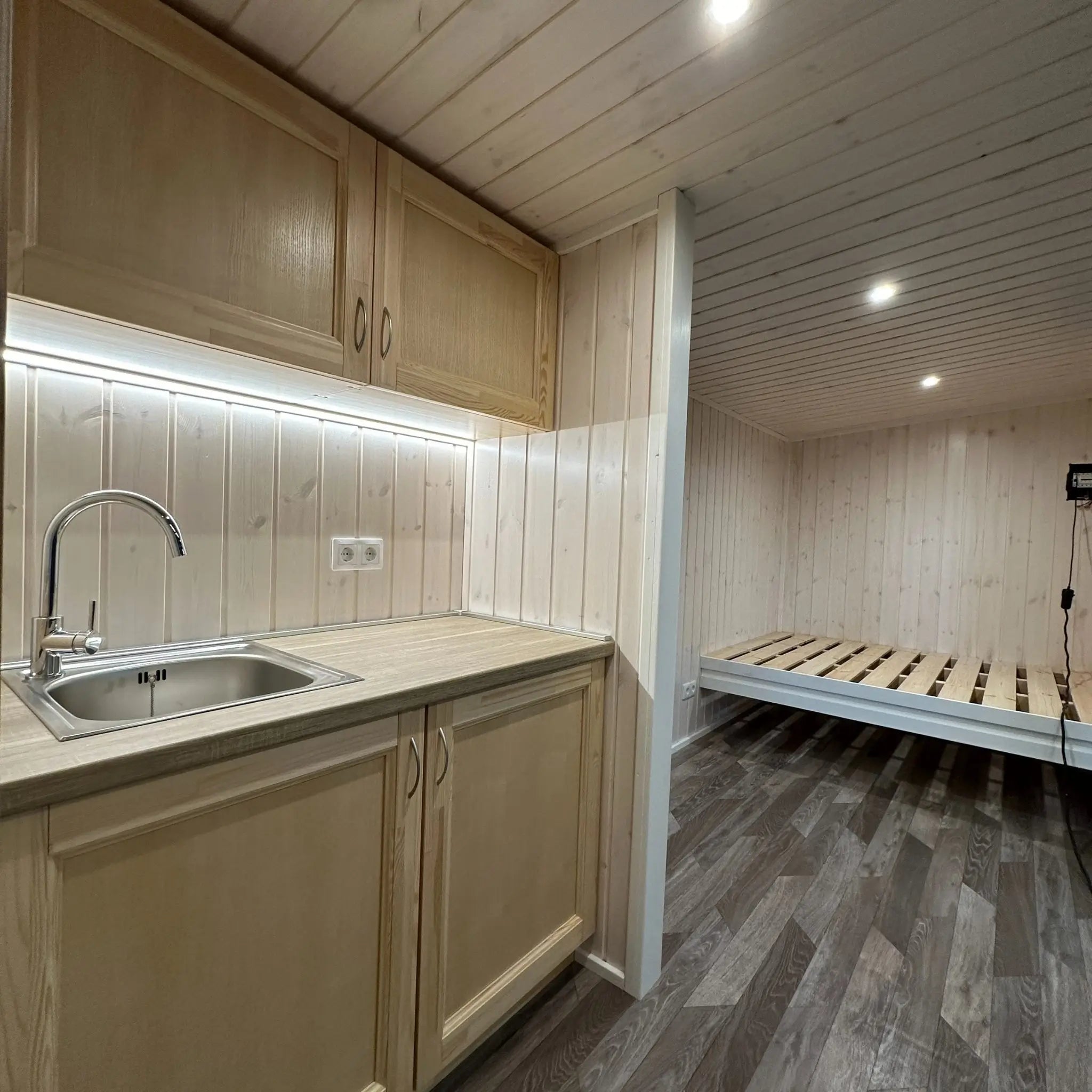 The Large GlampTainer container-style glamping unit – light timber kitchenette with LED strip lighting opposite built-in wooden bed frame