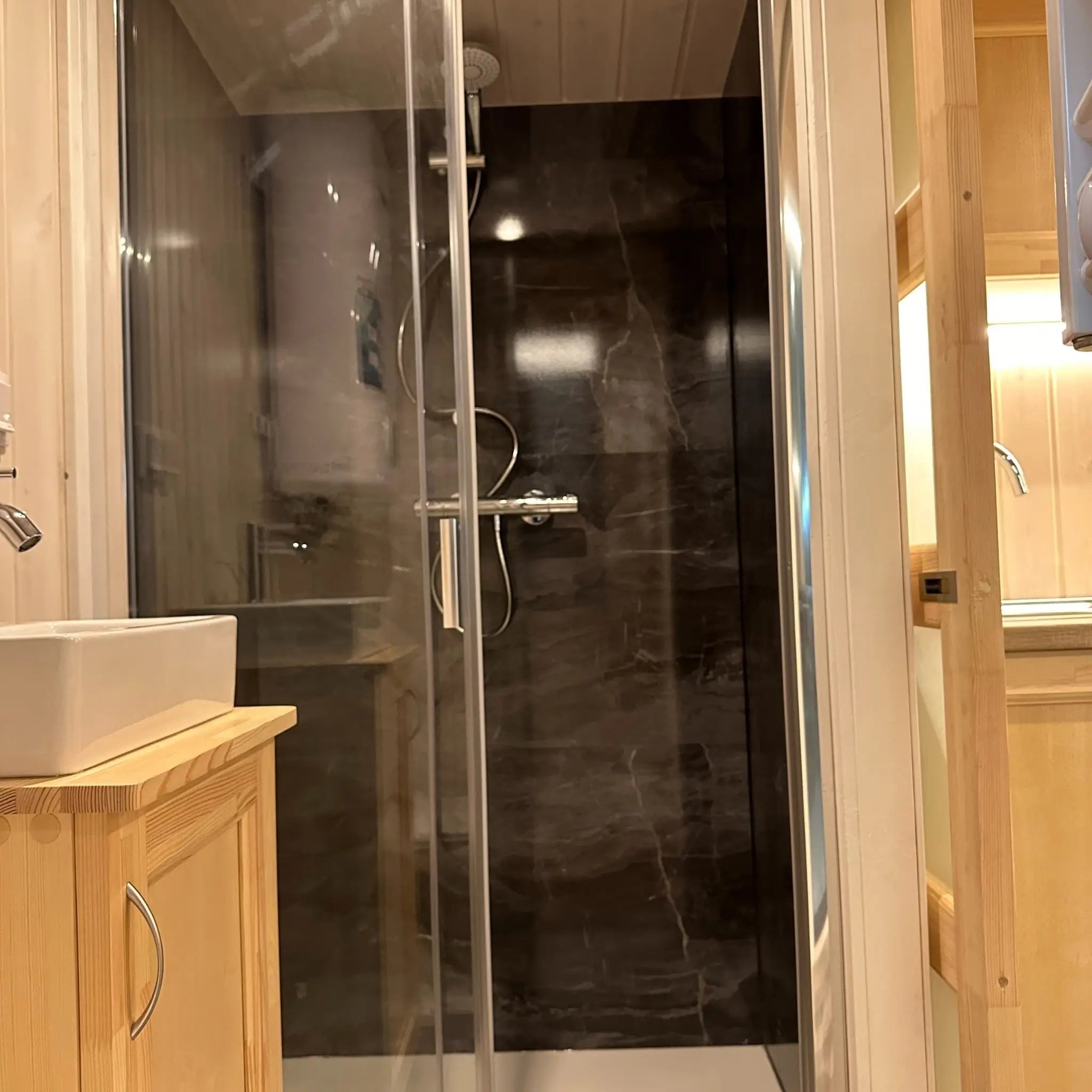 The Large GlampTainer container-style glamping unit – side view of compact vanity and modern standing shower in black-tiled bathroom