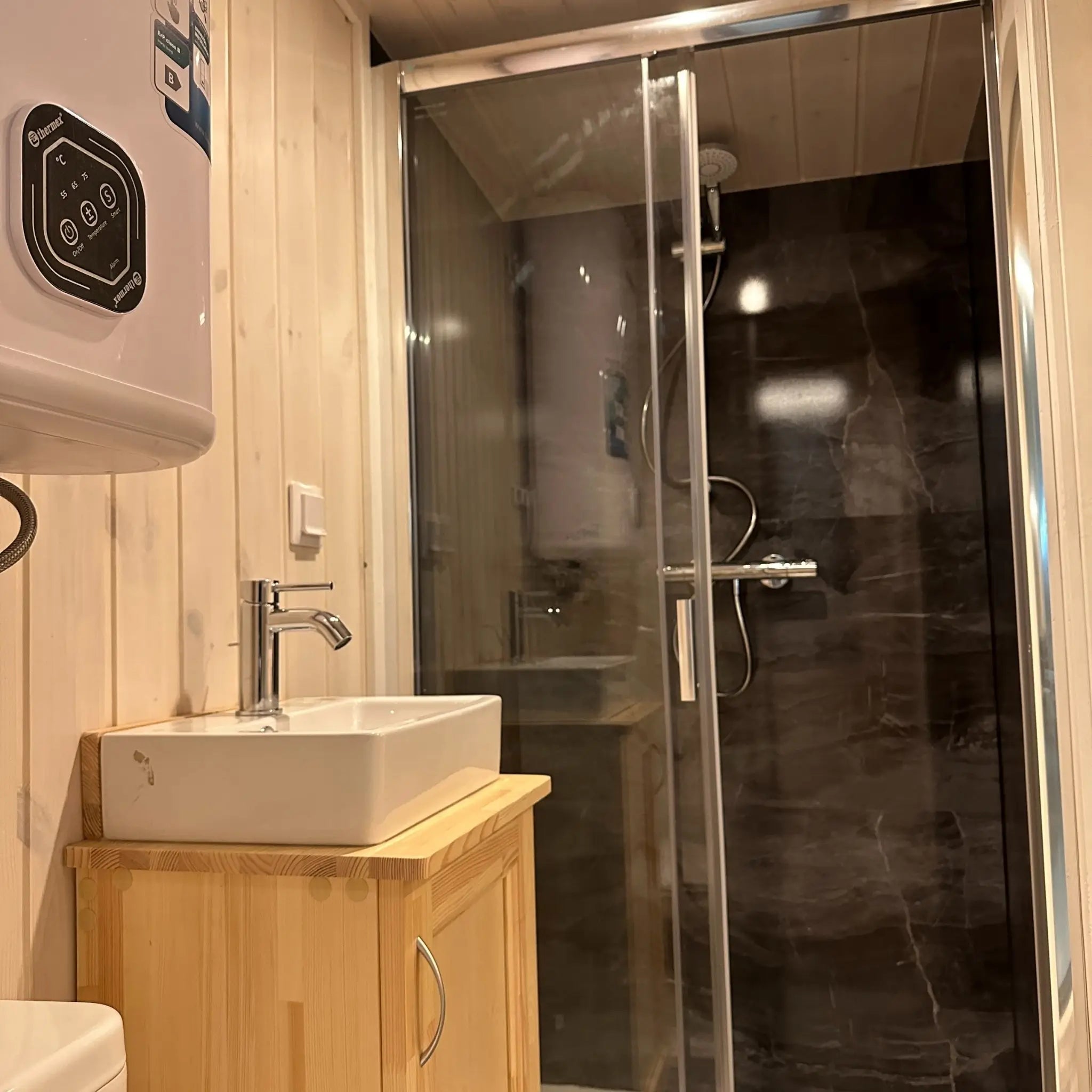 The Large GlampTainer container-style glamping unit – close-up of modern basin and glass-enclosed standing shower with dark stone-style wall