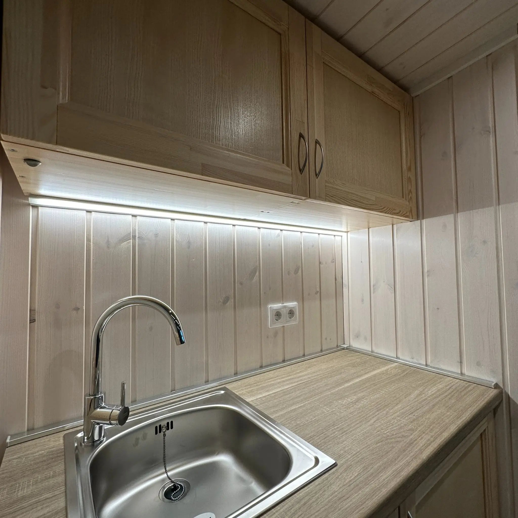 The Large GlampTainer container-style glamping unit – close-up of stainless steel sink with chrome tap set into timber countertop and LED lighting