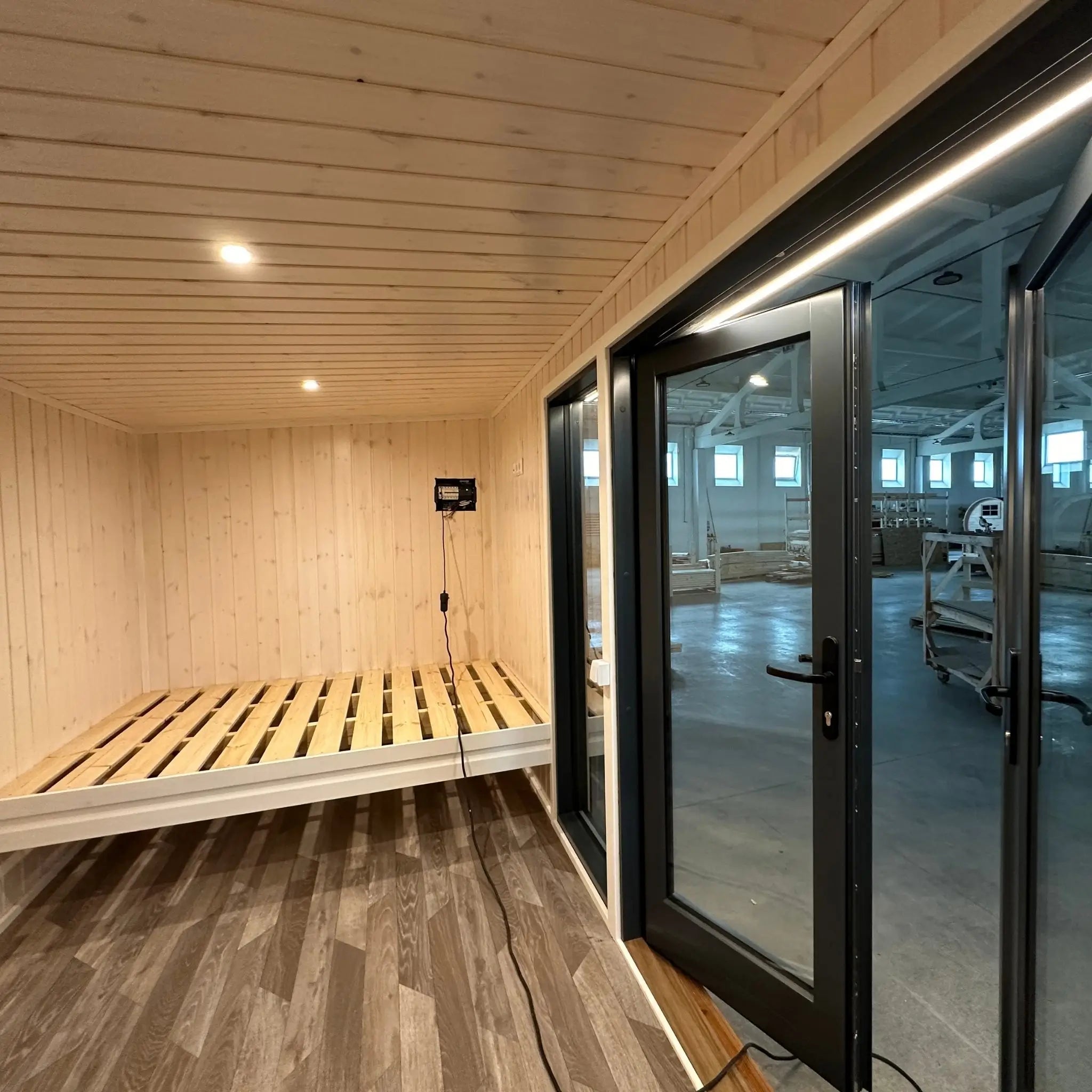 The Large GlampTainer container-style glamping unit – cozy sleeping area with raised wooden bed frame facing full-glass double doors