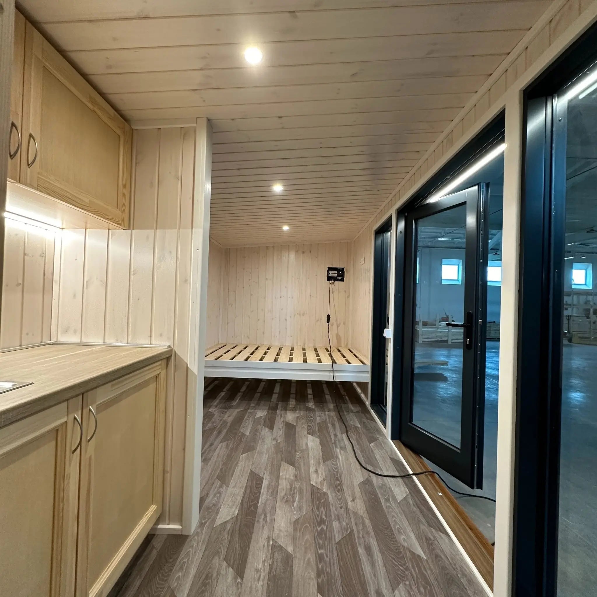 The Large GlampTainer container-style glamping unit – timber kitchenette with LED strip lighting opposite built-in wooden bed frame