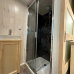 The Large GlampTainer container-style glamping unit – compact bathroom with dark-tiled standing shower and light wood vanity sink