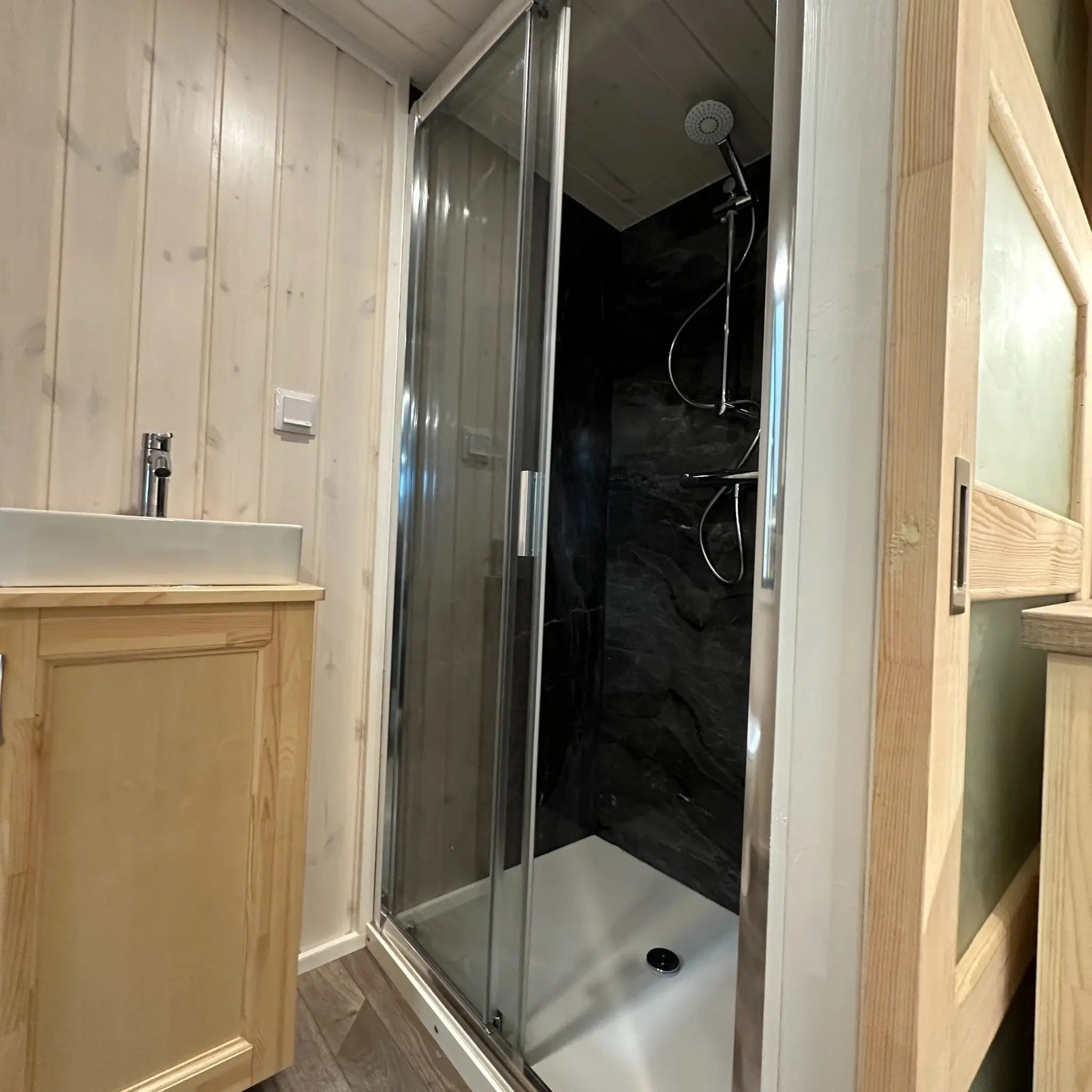 The Large GlampTainer container-style glamping unit – compact bathroom with dark-tiled standing shower and light wood vanity sink
