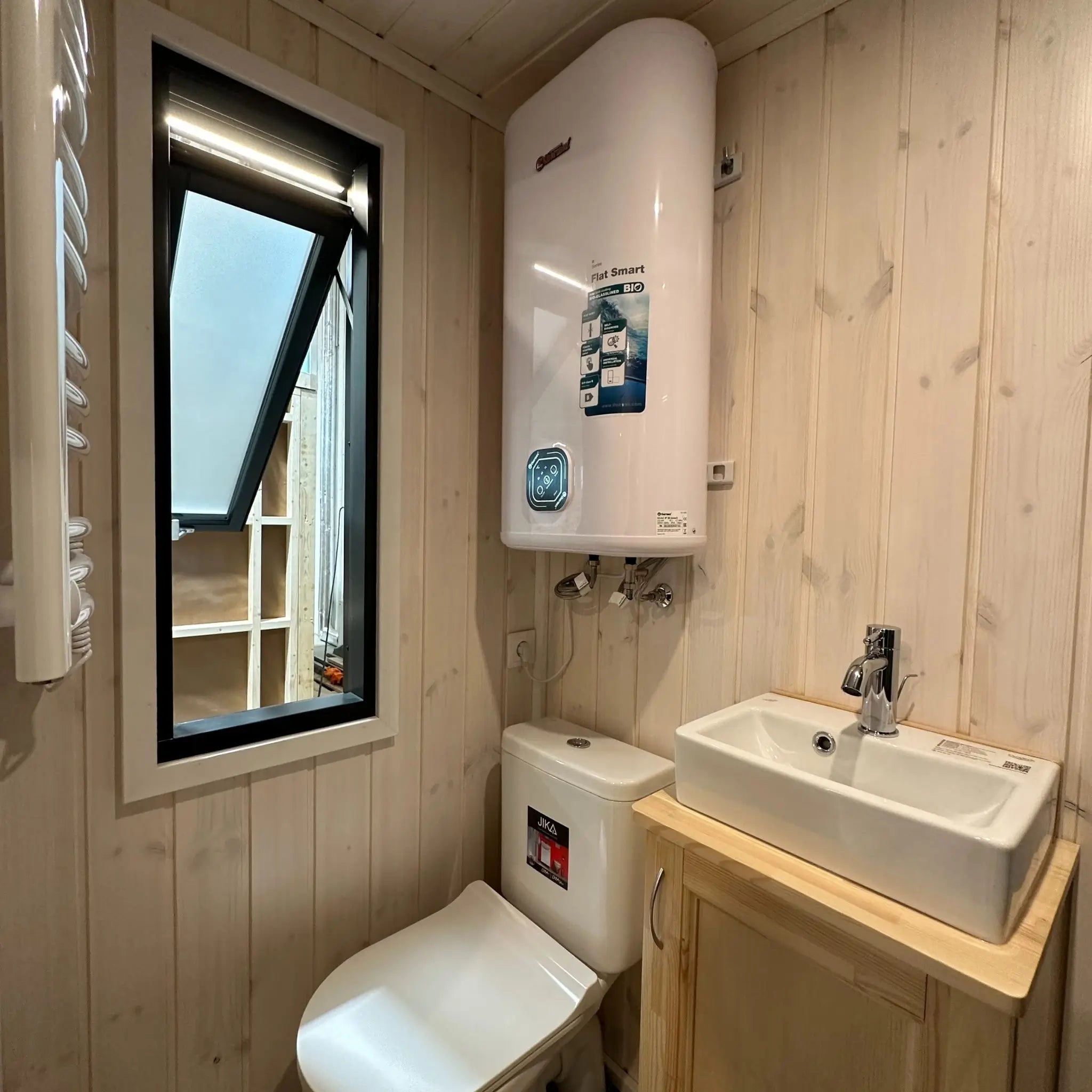 The Large GlampTainer container-style glamping unit – bathroom with vanity sink, toilet, heater and tall black-framed window