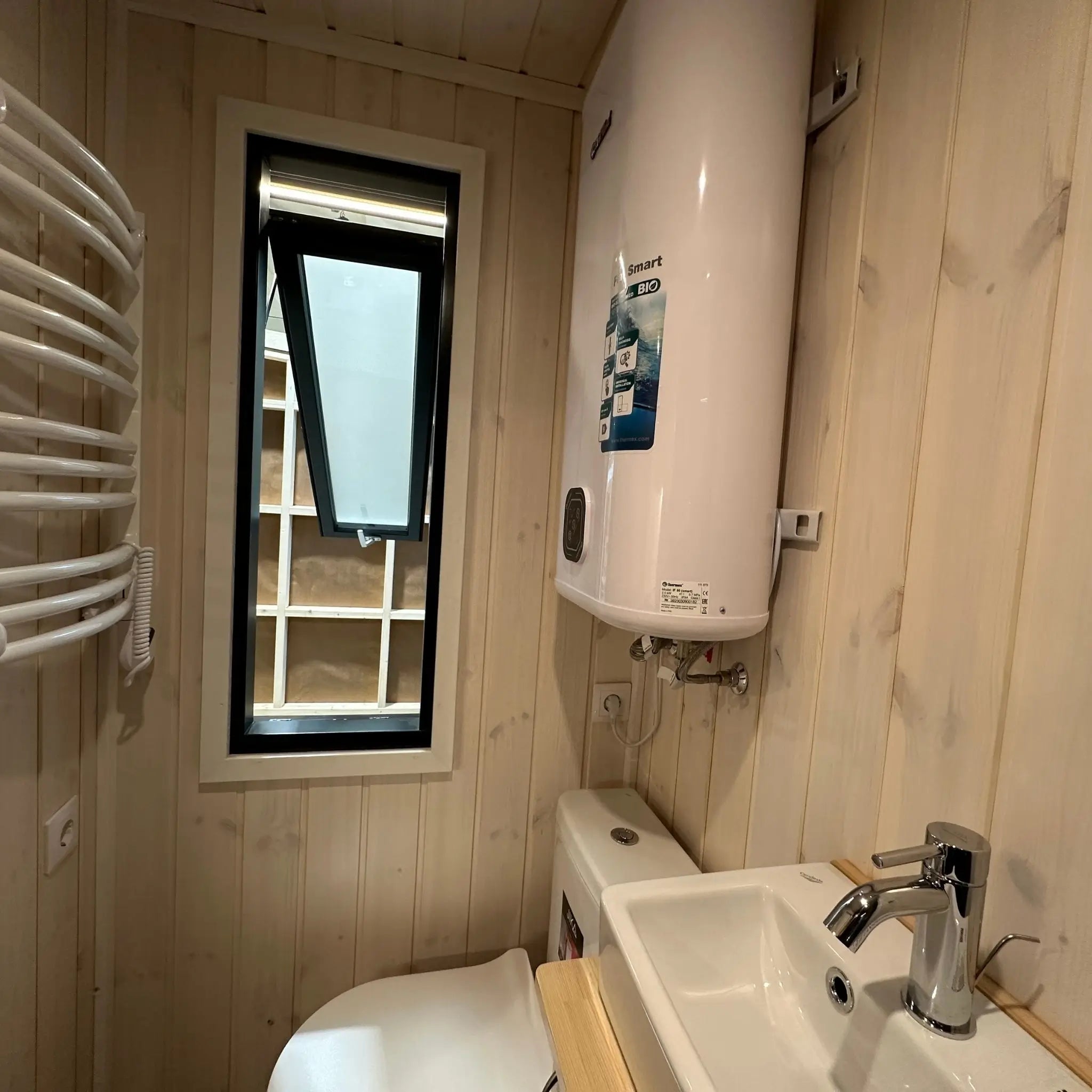 The Large GlampTainer container-style glamping unit – side view of bathroom with toilet, water heater, and tall opened window