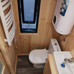 The Medium GlampTainer container-style glamping structure – small bathroom with wood panel walls, slim window, toilet and basin neatly fitted in a narrow layout