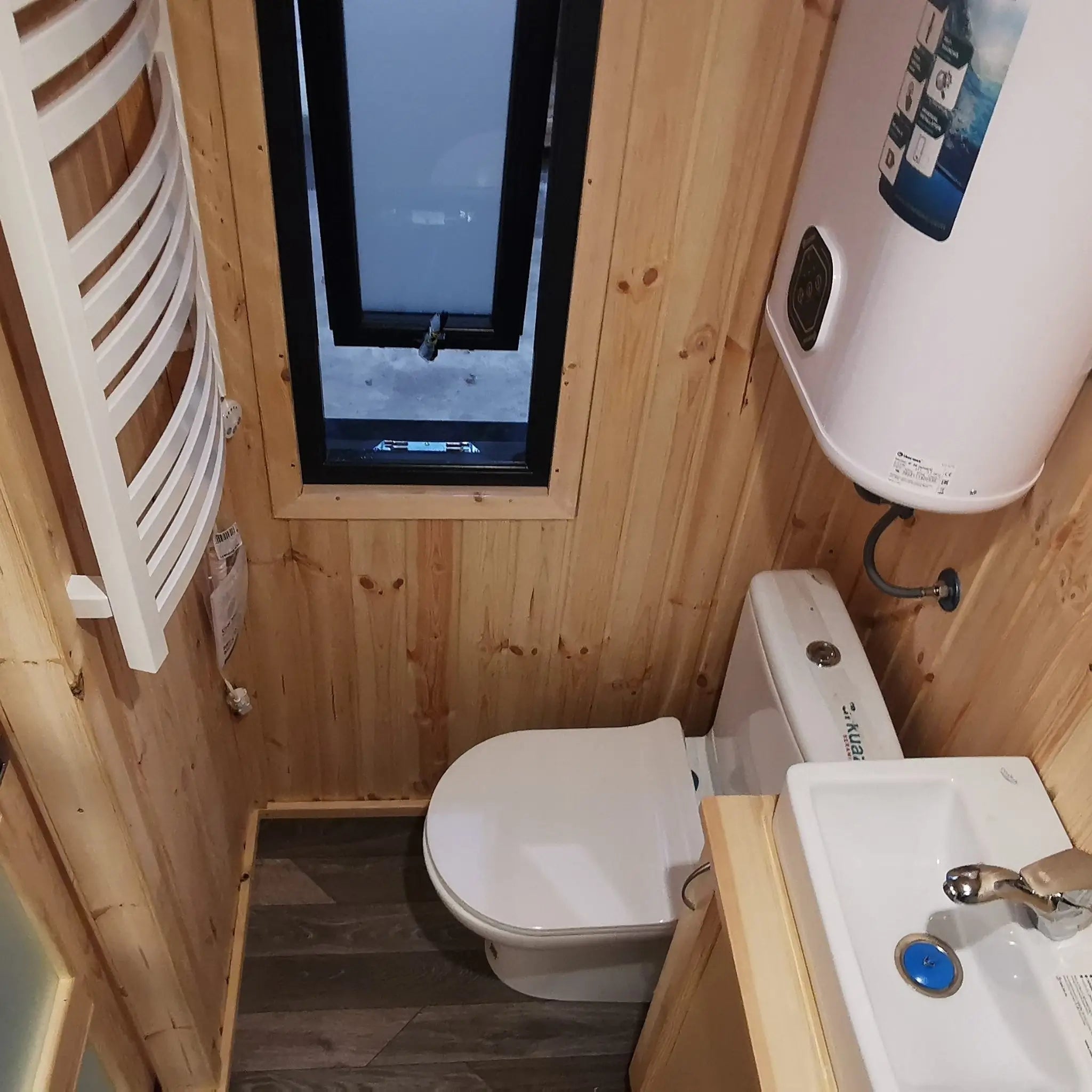 The Medium GlampTainer container-style glamping structure – small bathroom with wood panel walls, slim window, toilet and basin neatly fitted in a narrow layout