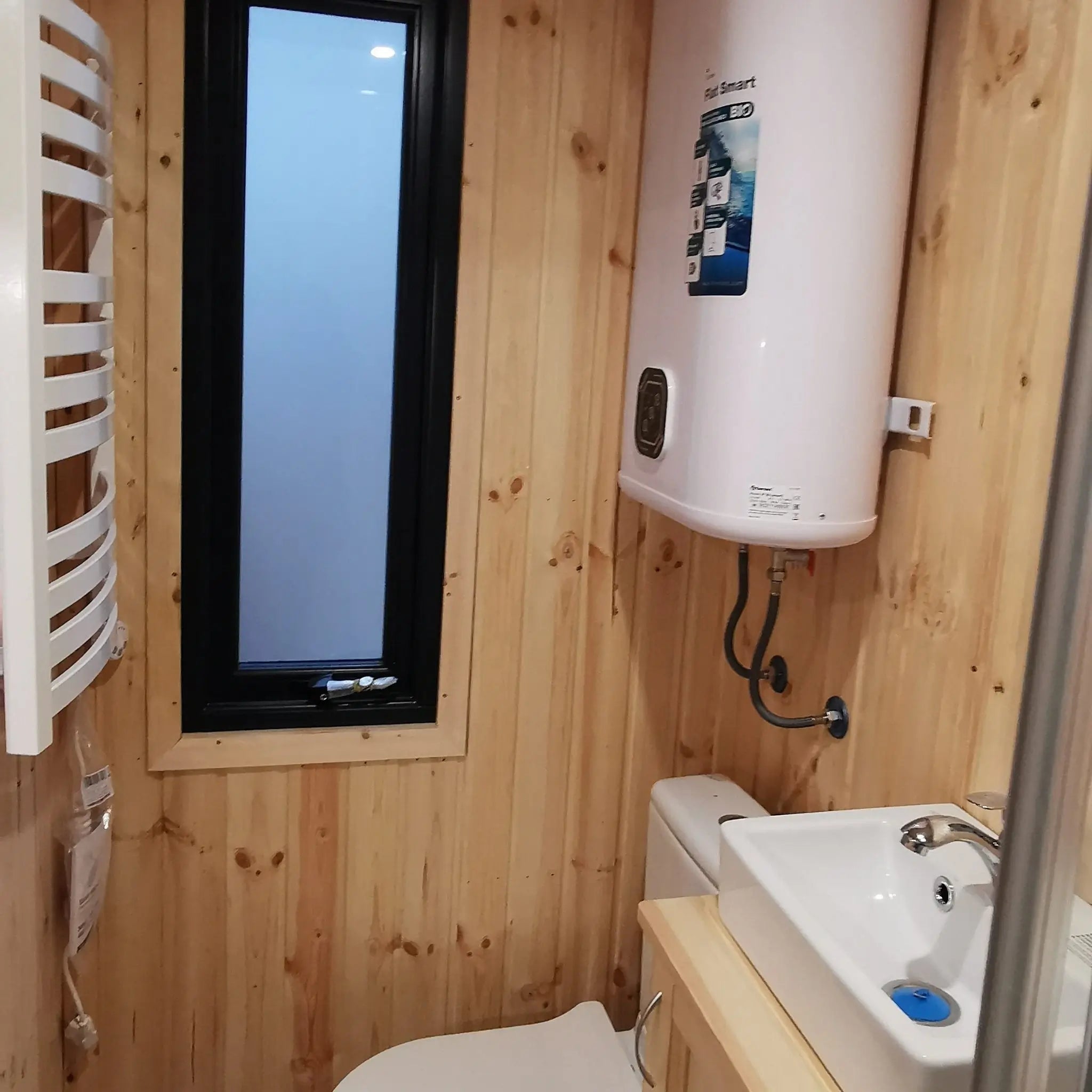 The Medium GlampTainer container-style glamping structure – compact bathroom with vertical window, towel dryer, and wall-mounted water heater on timber-clad walls