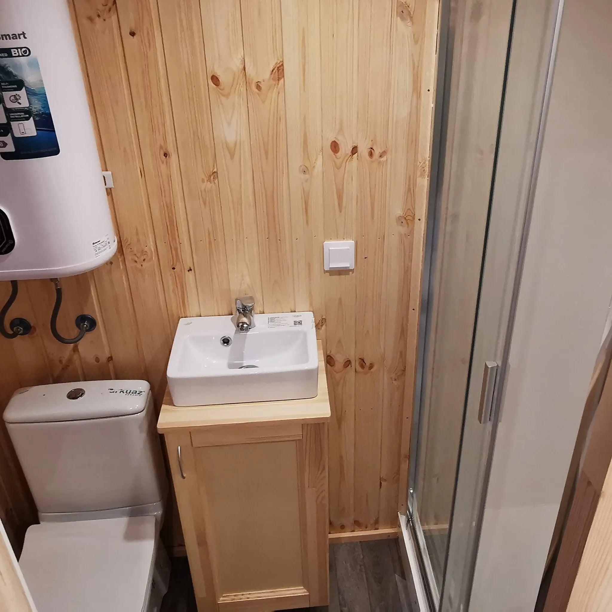 The Medium GlampTainer container-style glamping structure – top view of compact bathroom featuring toilet, vanity sink, and wall-mounted water heater in pine-clad space