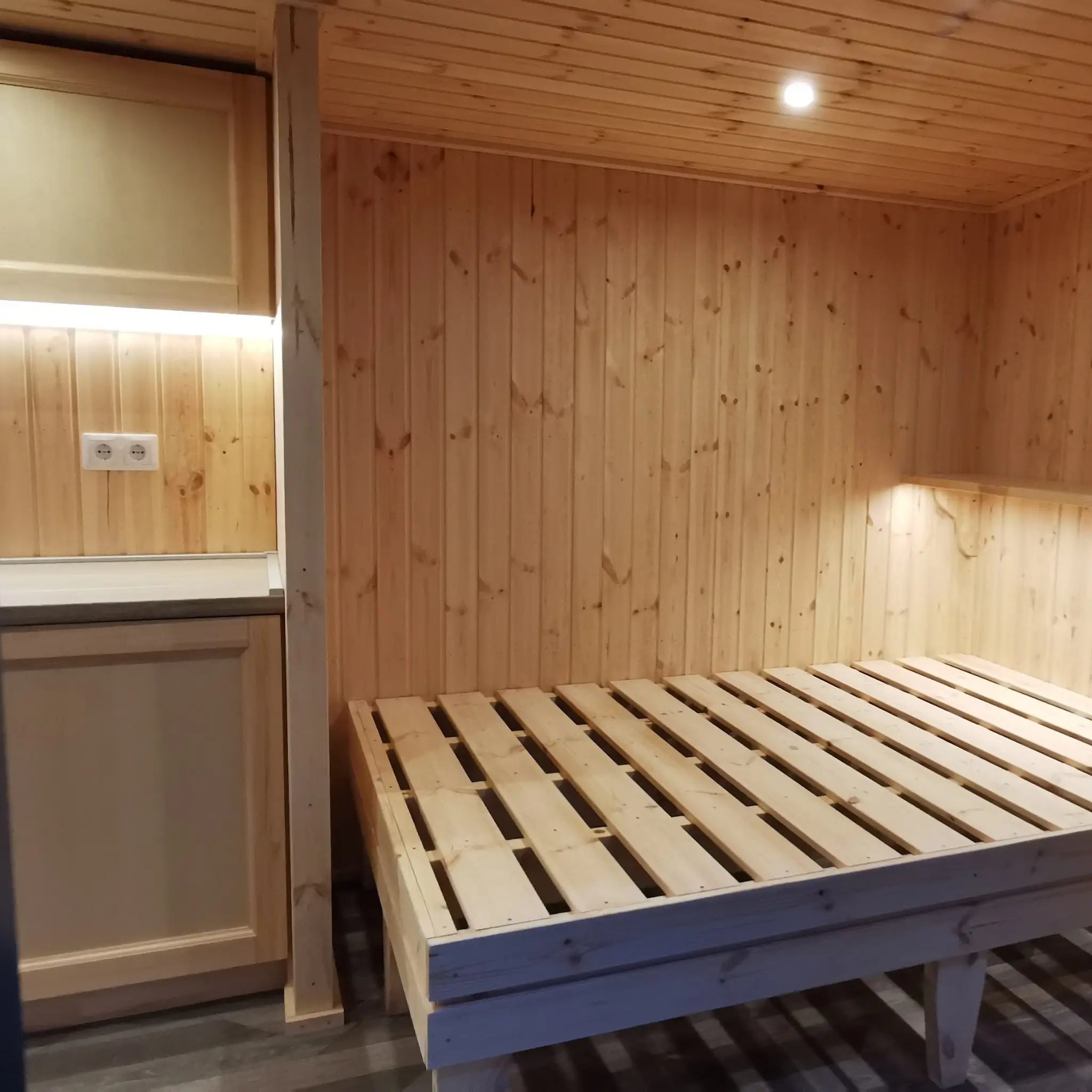 The Medium GlampTainer container-style glamping structure – wooden bed frame beneath recessed ceiling spotlights in a timber-lined cabin space