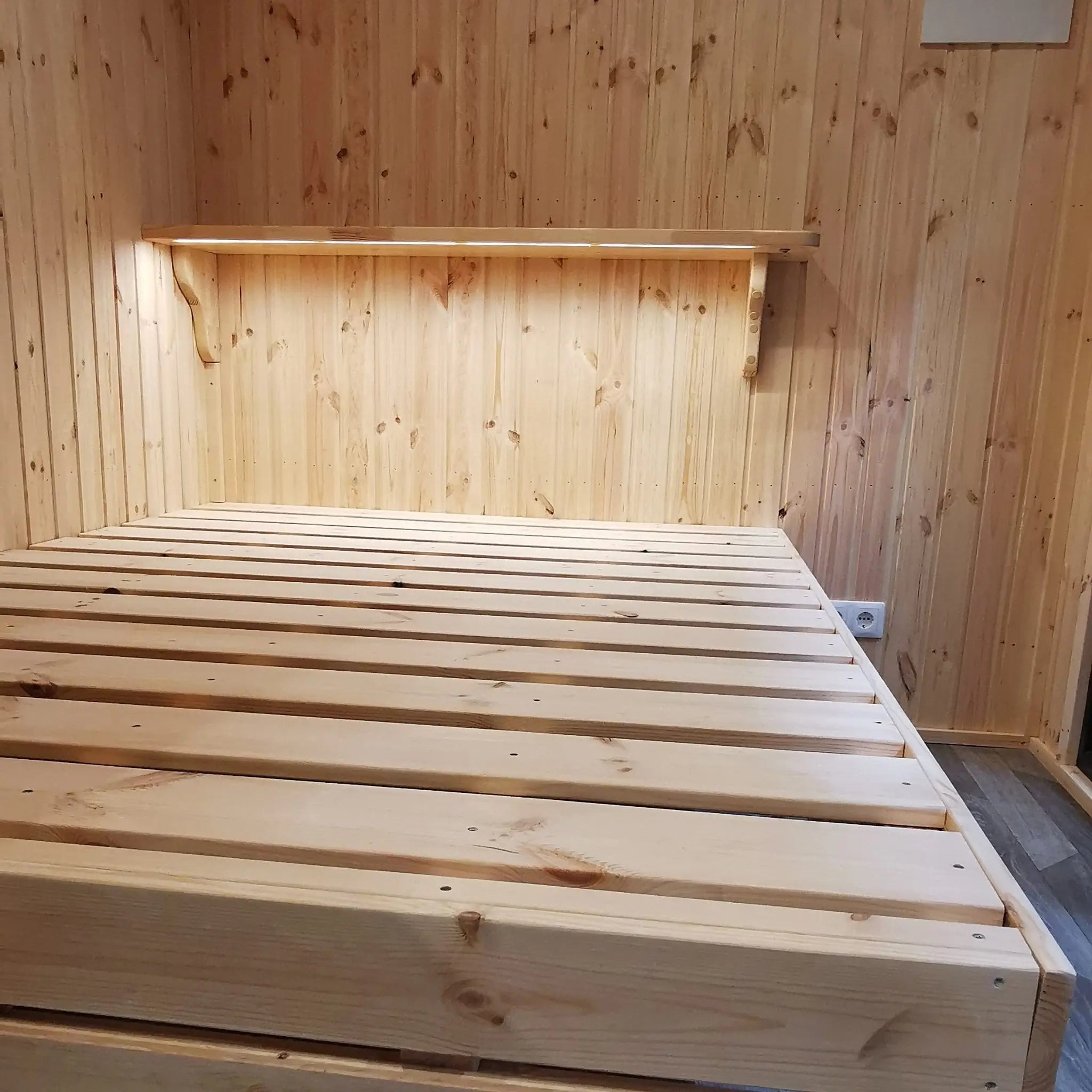 The Medium GlampTainer container-style glamping structure – space-saving bedroom with raised bed frame and slim timber shelf on the feature wall