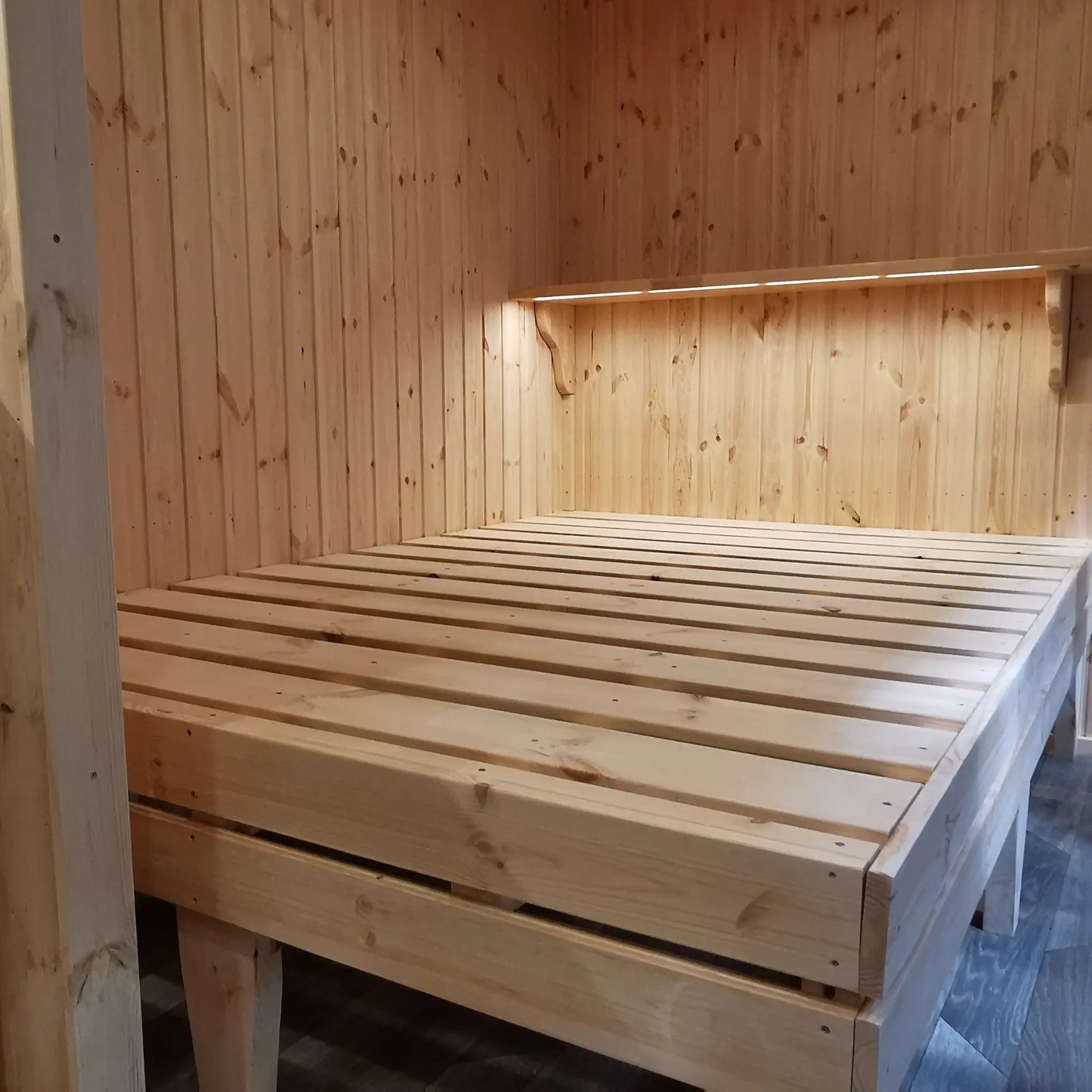 The Medium GlampTainer container-style glamping structure – minimalist bedroom with raised wooden bed and slim wall-mounted shelf above the headboard