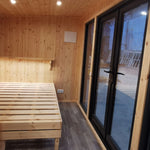 The Medium GlampTainer container-style glamping structure – cozy bedroom with built-in wooden bed frame and full-height glass doors opening to the outdoors