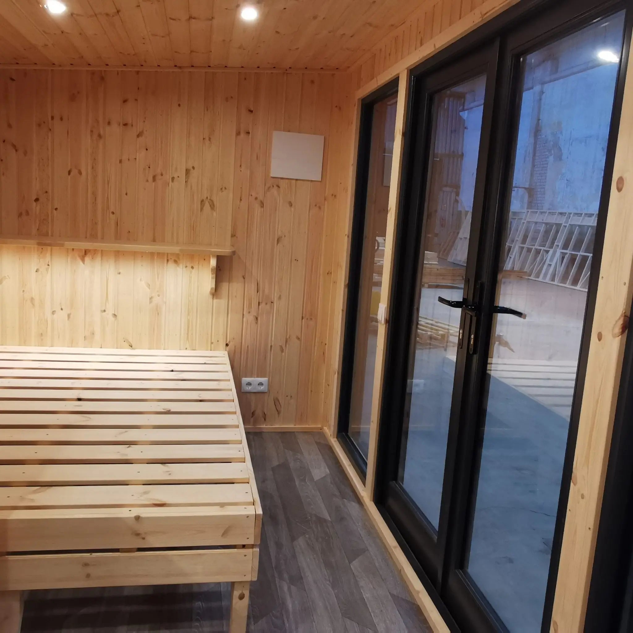 The Medium GlampTainer container-style glamping structure – cozy bedroom with built-in wooden bed frame and full-height glass doors opening to the outdoors