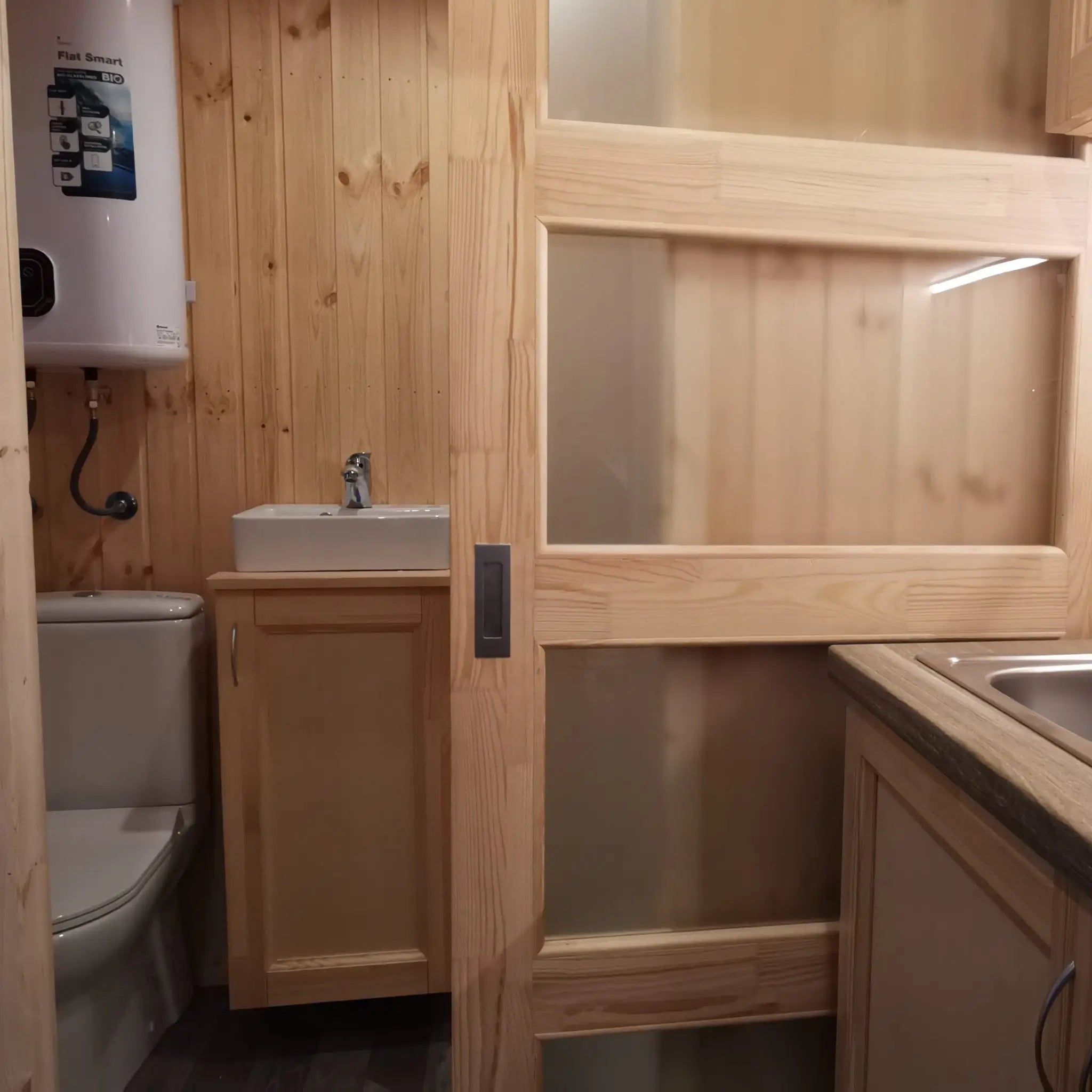The Medium GlampTainer container-style glamping structure – compact bathroom with toilet and basin seen through sliding door beside kitchen counter