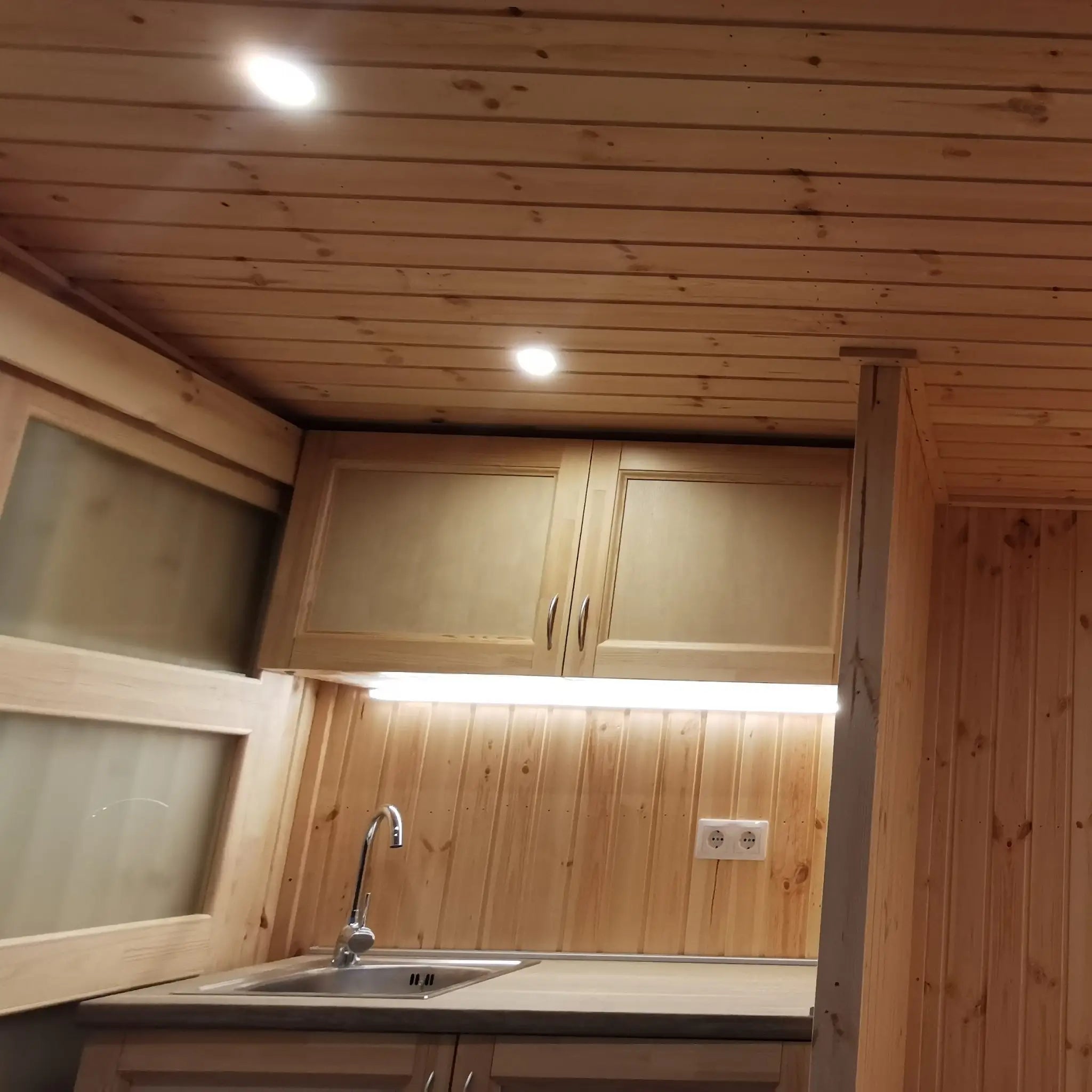 The Medium GlampTainer container-style glamping structure – compact kitchenette with overhead cabinets, under-cabinet LED lighting and timber ceiling panels