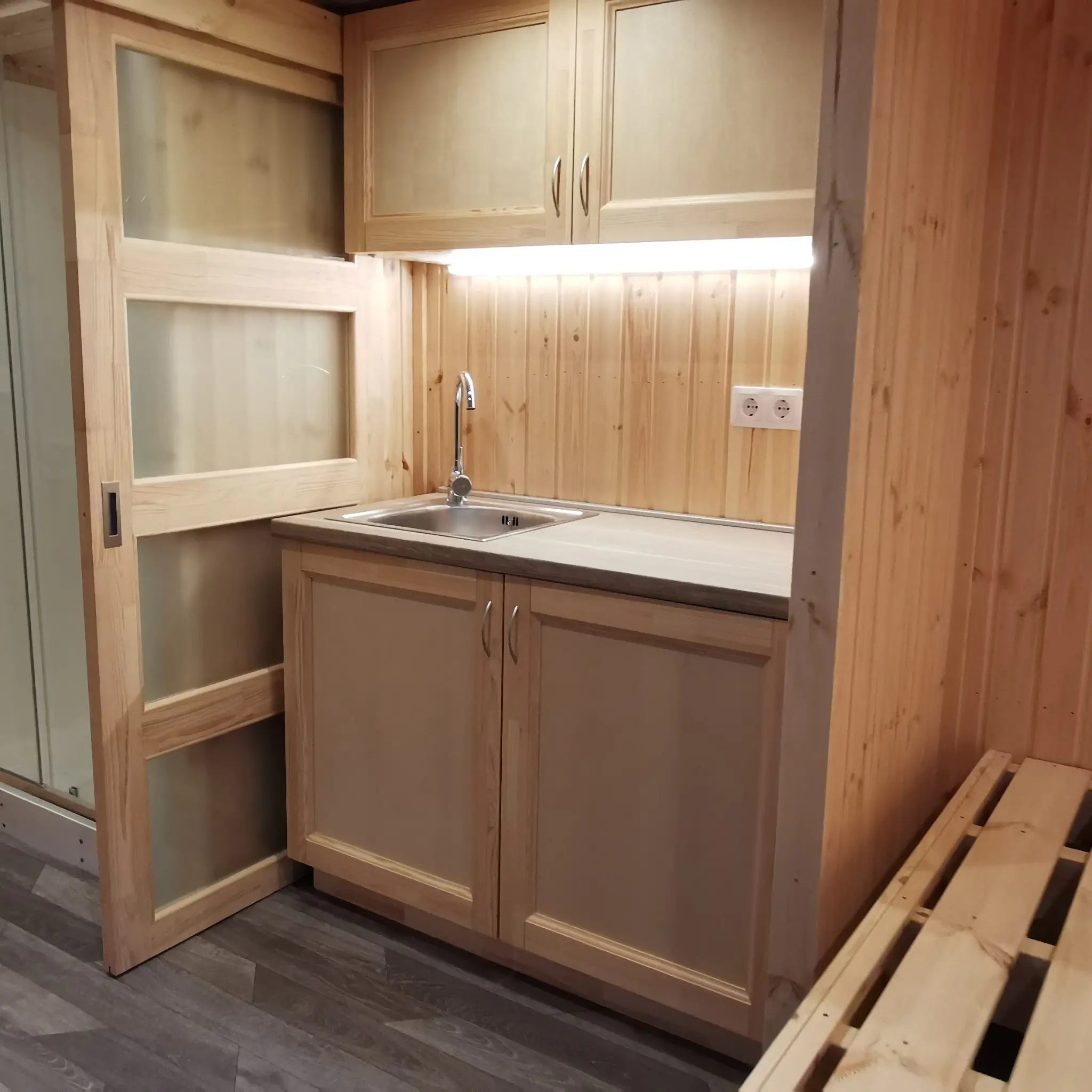 The Medium GlampTainer container-style glamping structure – minimalist kitchenette with warm wood cabinets, overhead lighting and sink