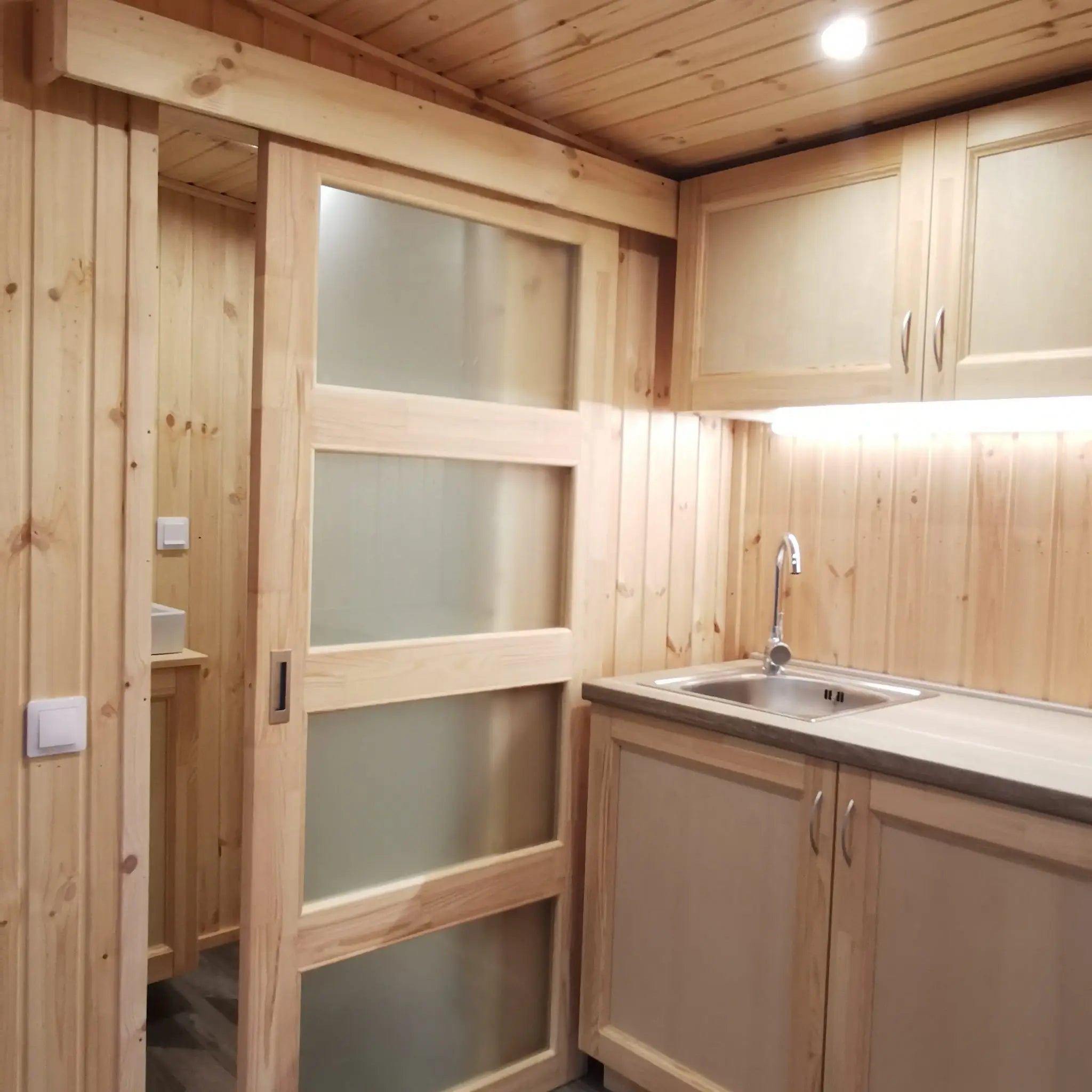 The Medium GlampTainer container-style glamping structure – kitchenette with sliding frosted door leading into compact bathroom