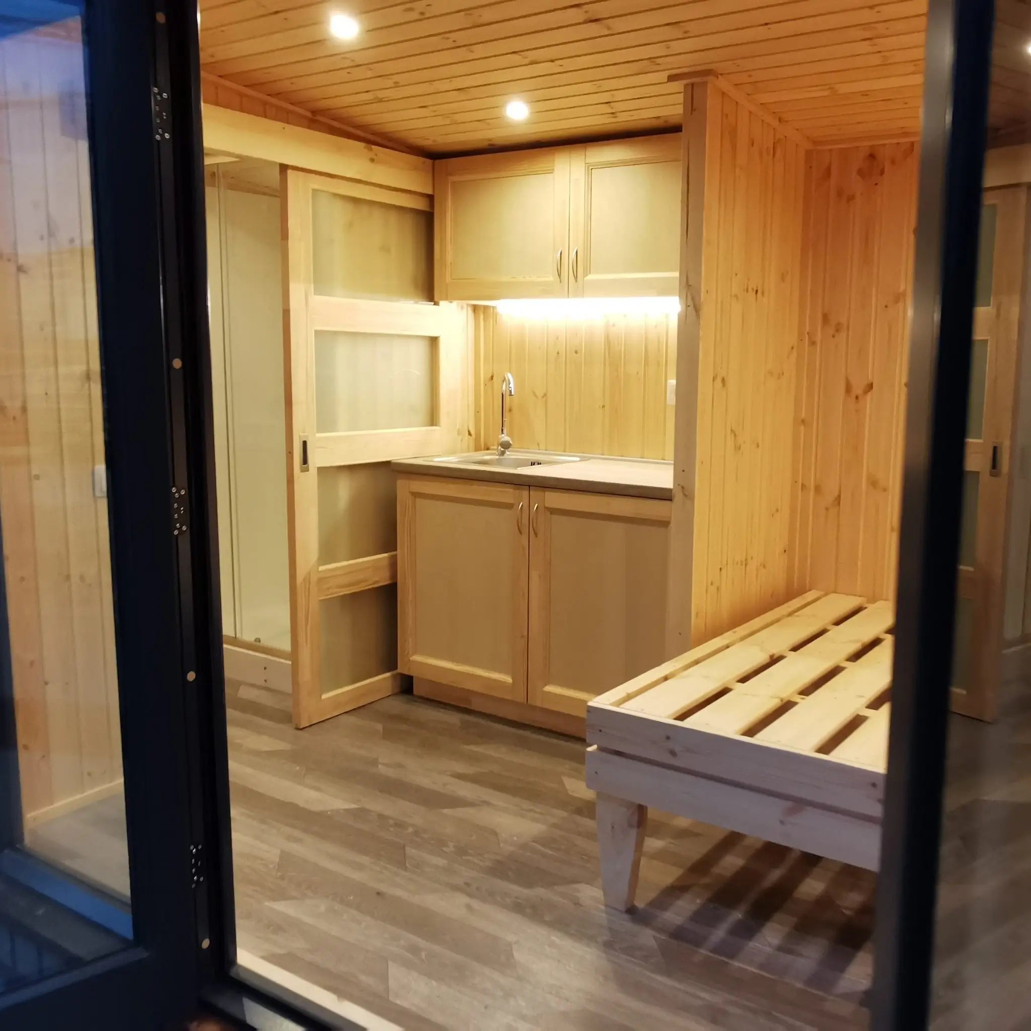 The Medium GlampTainer container-style glamping structure – smart space-saving design with wooden bed frame next to compact kitchenette