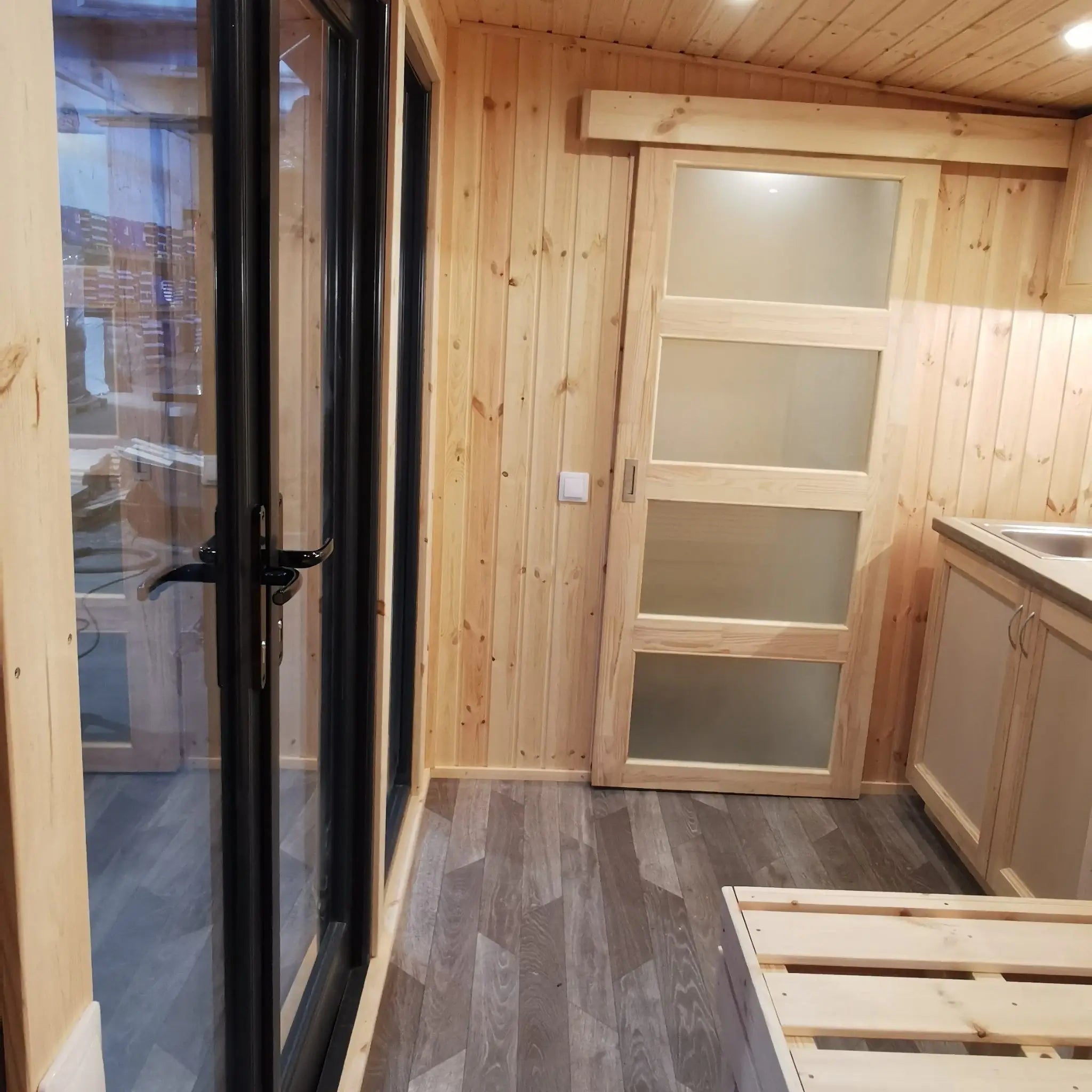 The Medium GlampTainer container-style glamping structure – inviting open-plan interior with full-glass front doors, bed platform and kitchenette