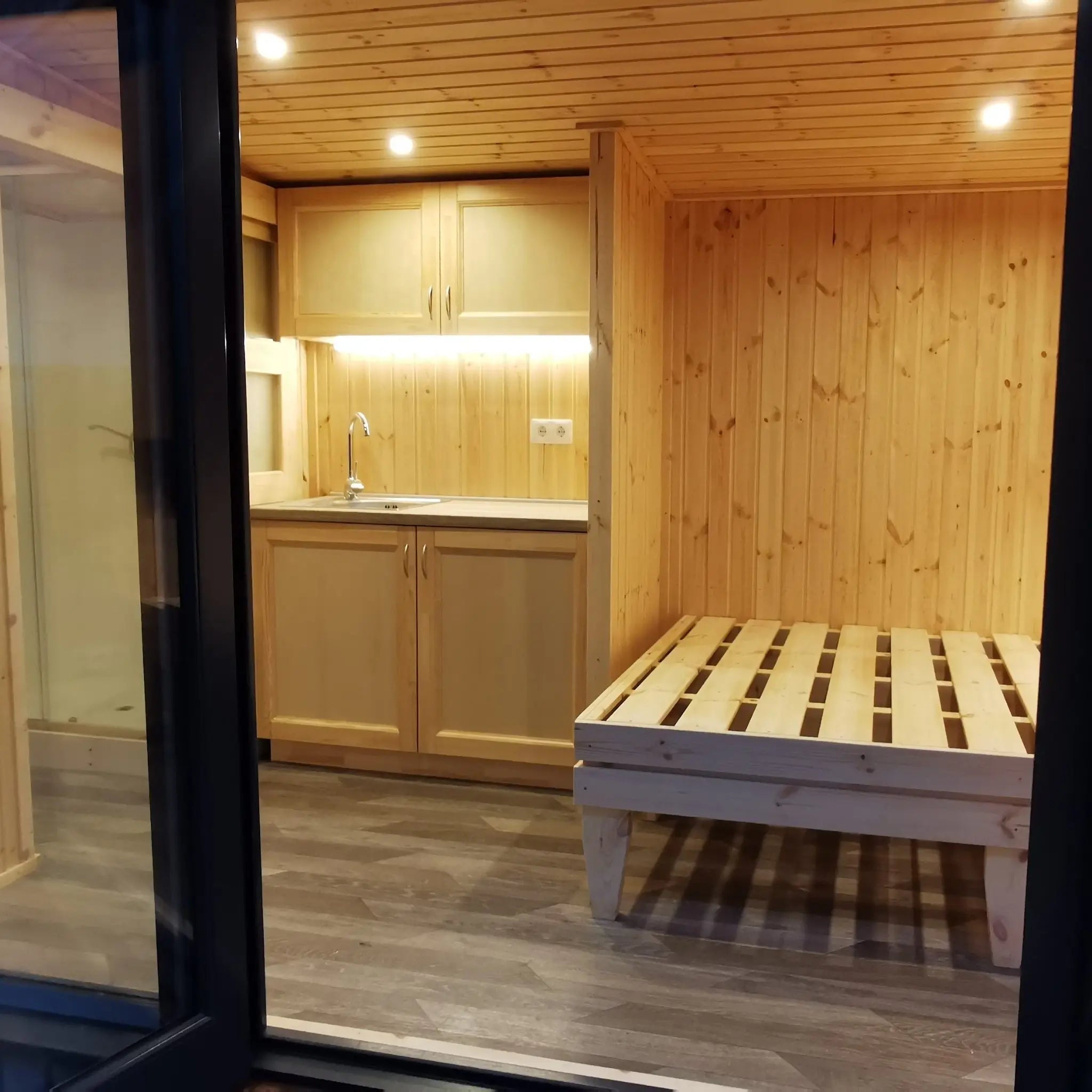 The Medium GlampTainer container-style glamping structure – cozy interior with compact kitchenette and built-in wooden bed viewed from entrance