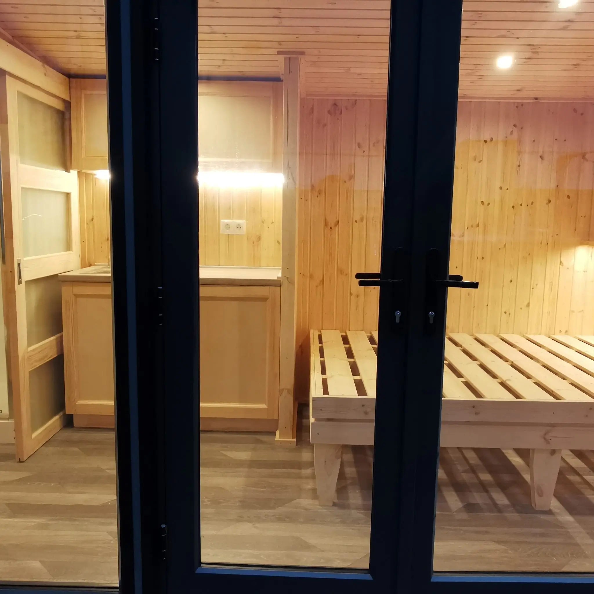 The Medium GlampTainer container-style glamping structure – compact kitchenette with LED strip lighting and overhead cabinets seen through side window