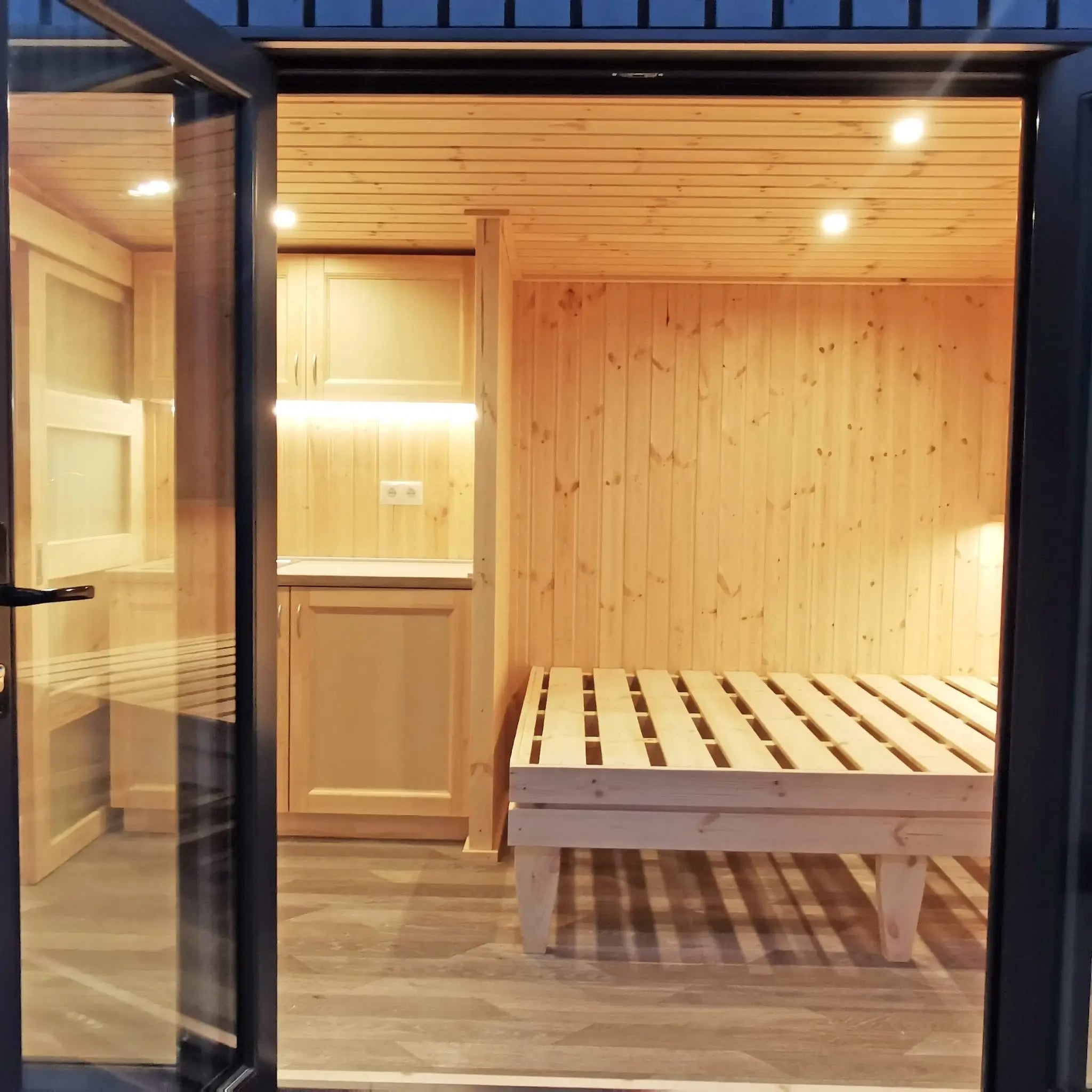 The Medium GlampTainer container-style glamping structure – cozy interior with compact kitchenette and built-in wooden bed viewed from entrance