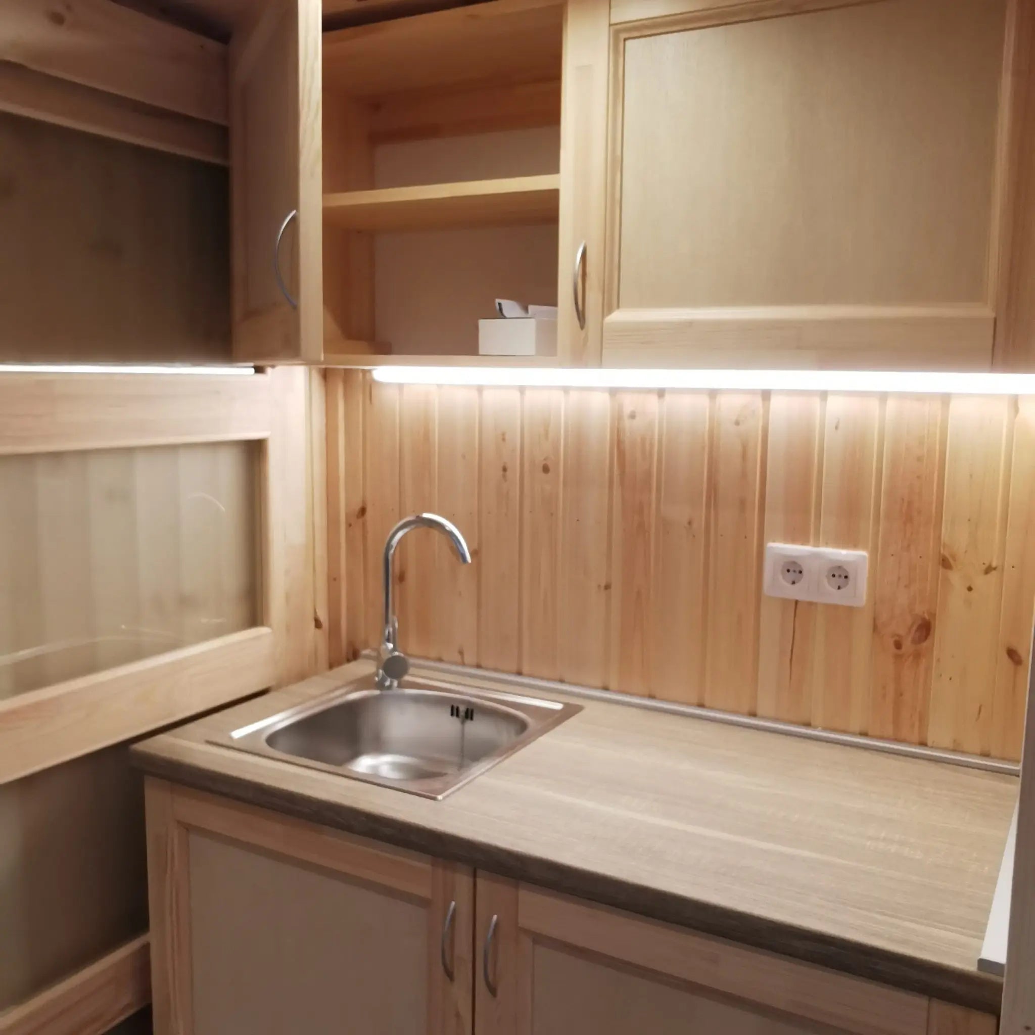 The Medium GlampTainer container-style glamping structure – close-up of wooden kitchenette with open wall-mounted cabinet and modern tap