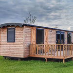 Side view of luxury shepherd’s hut with wooden cladding, private decking and outdoor seating area