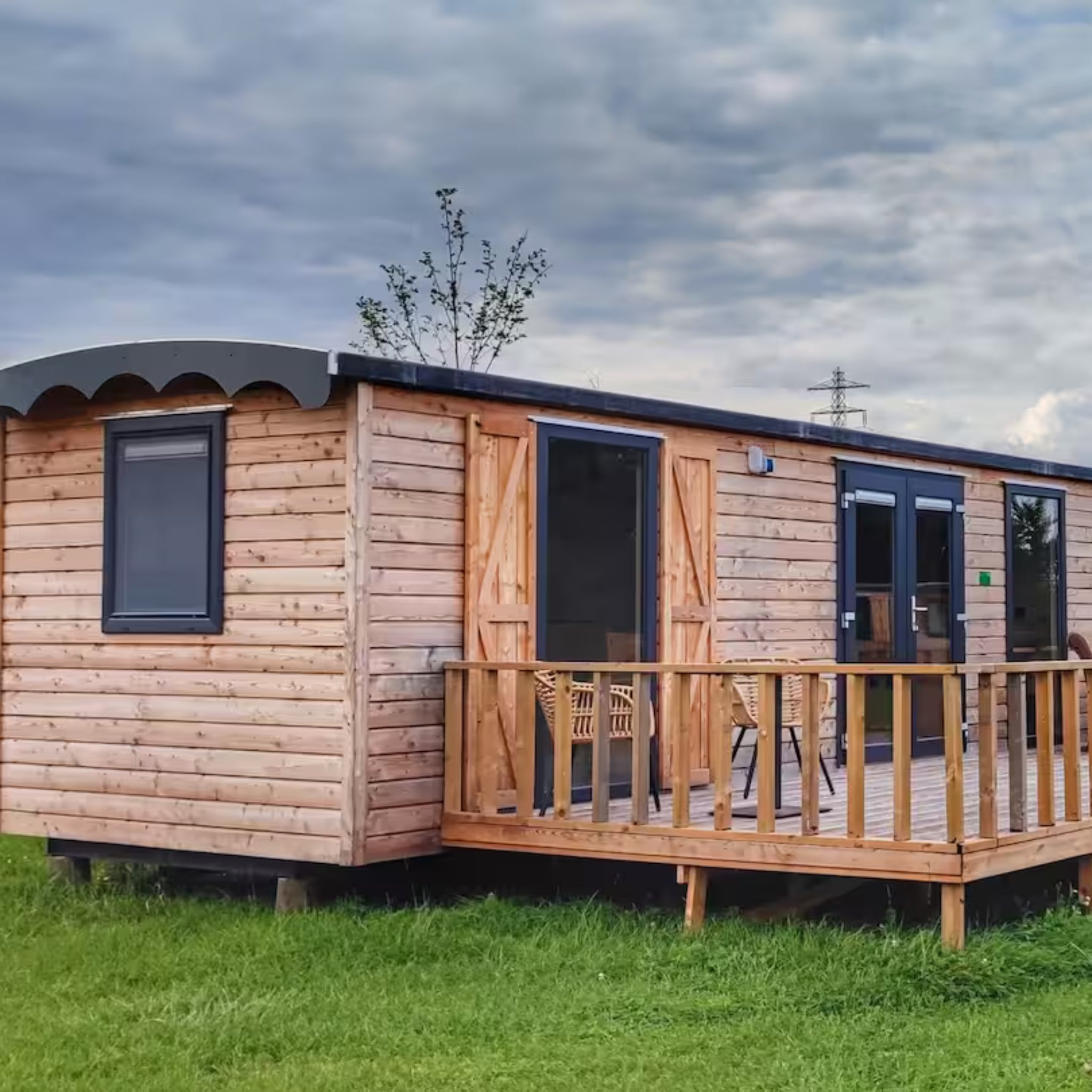 Side view of luxury shepherd’s hut with wooden cladding, private decking and outdoor seating area