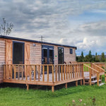 Angled exterior view of modern shepherd’s hut with wraparound decking in rural surroundings