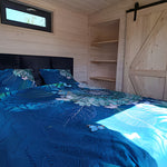 Cozy bedroom inside luxury shepherd’s hut with double bed, shelving and rustic wood interior