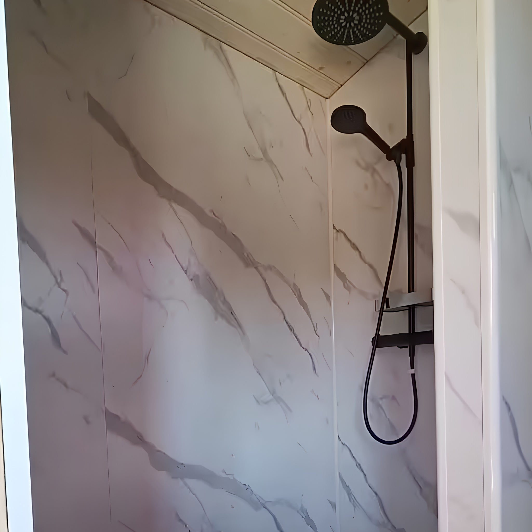 Contemporary shower room inside luxury shepherd’s hut with marble-effect walls and black fittings