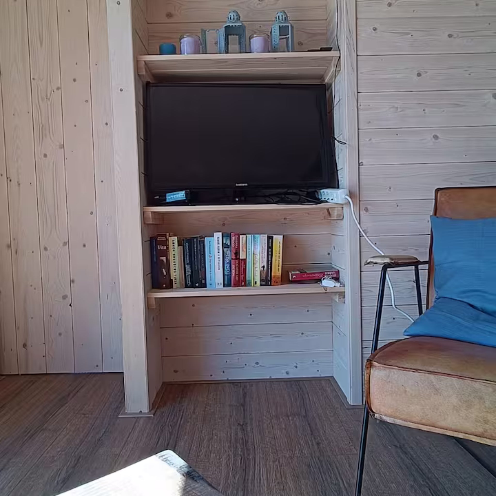 Interior TV and shelving area inside shepherd’s hut with books and rustic wood finish