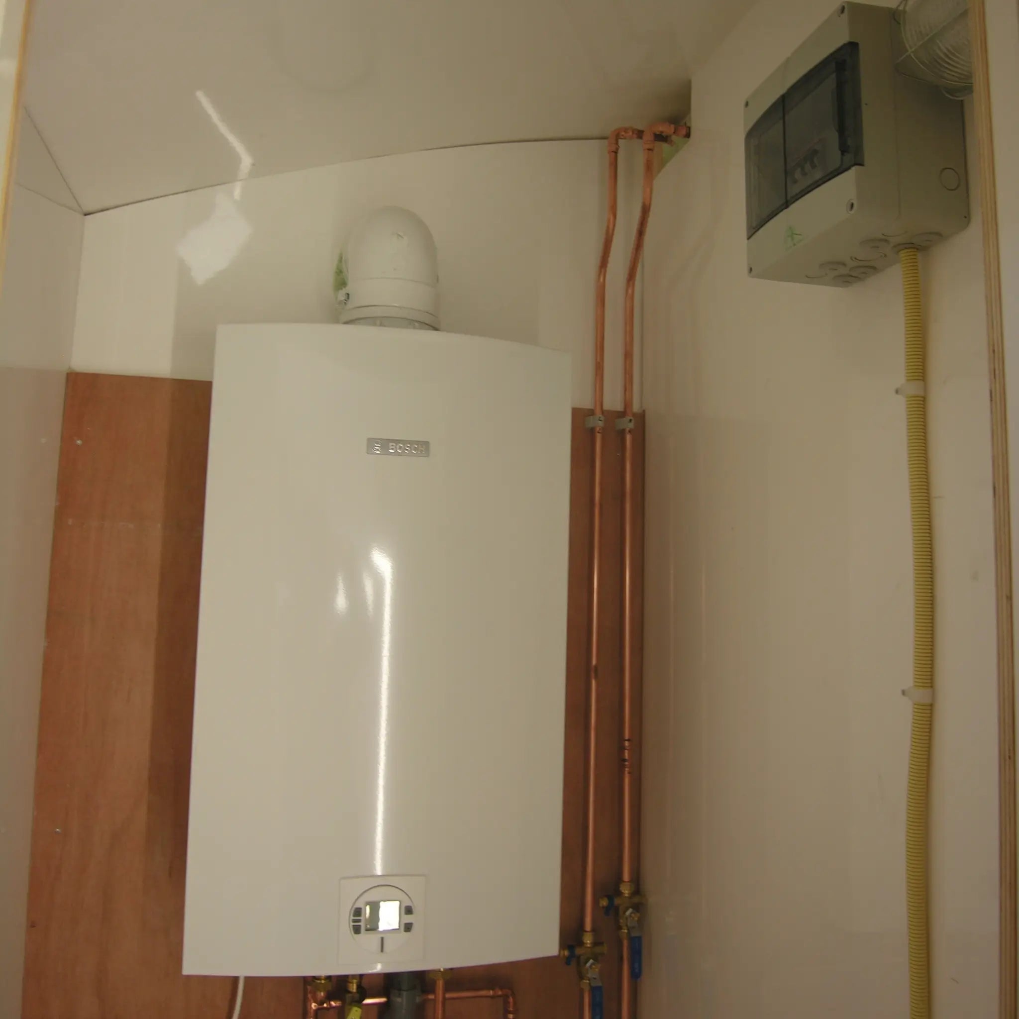 Compact Bosch water heater and utility connections installed inside shepherds hut technical room