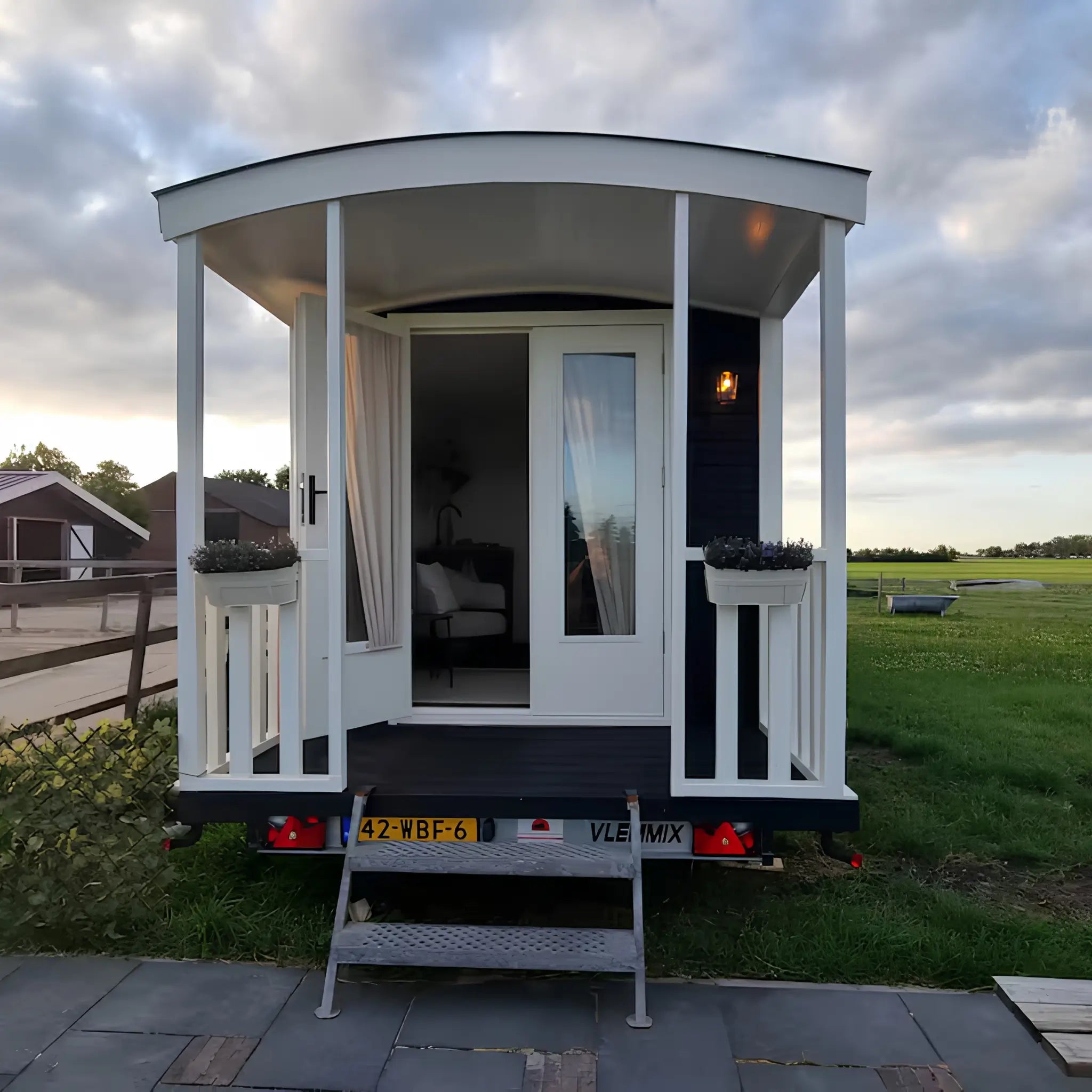 Front view of luxury shepherd’s hut with covered porch, curved roof, white decking, and modern tiny house design.