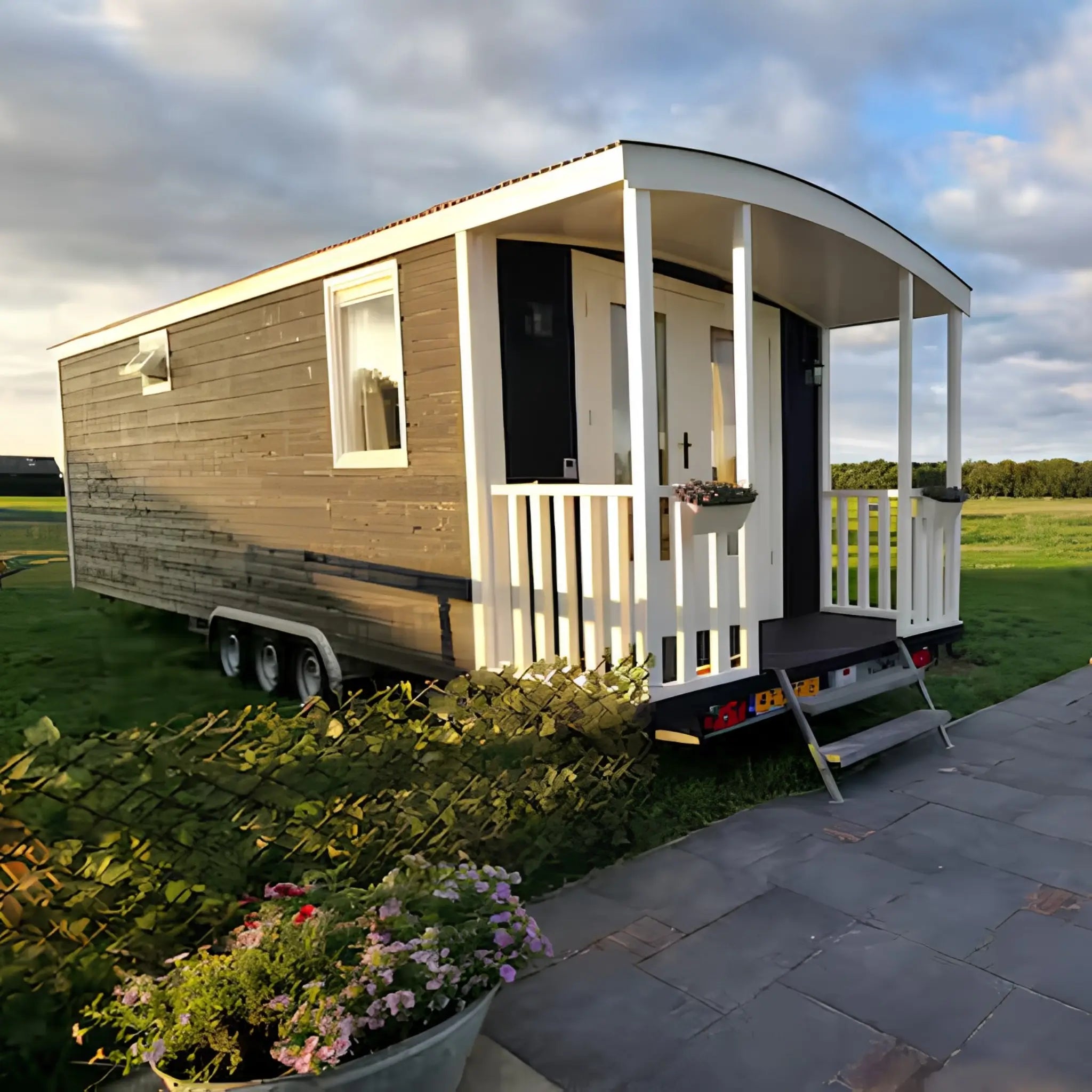 Exterior side profile of modern shepherd’s hut with black timber cladding, curved roof, front veranda, and scenic rural surroundings.