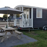 Side view of luxury shepherd’s hut beside an outdoor picnic table and parasol in a peaceful glamping setting.