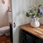 Rustic bathroom entrance with sliding barn door, wooden countertops, and floral decor inside a luxury shepherd’s hut.