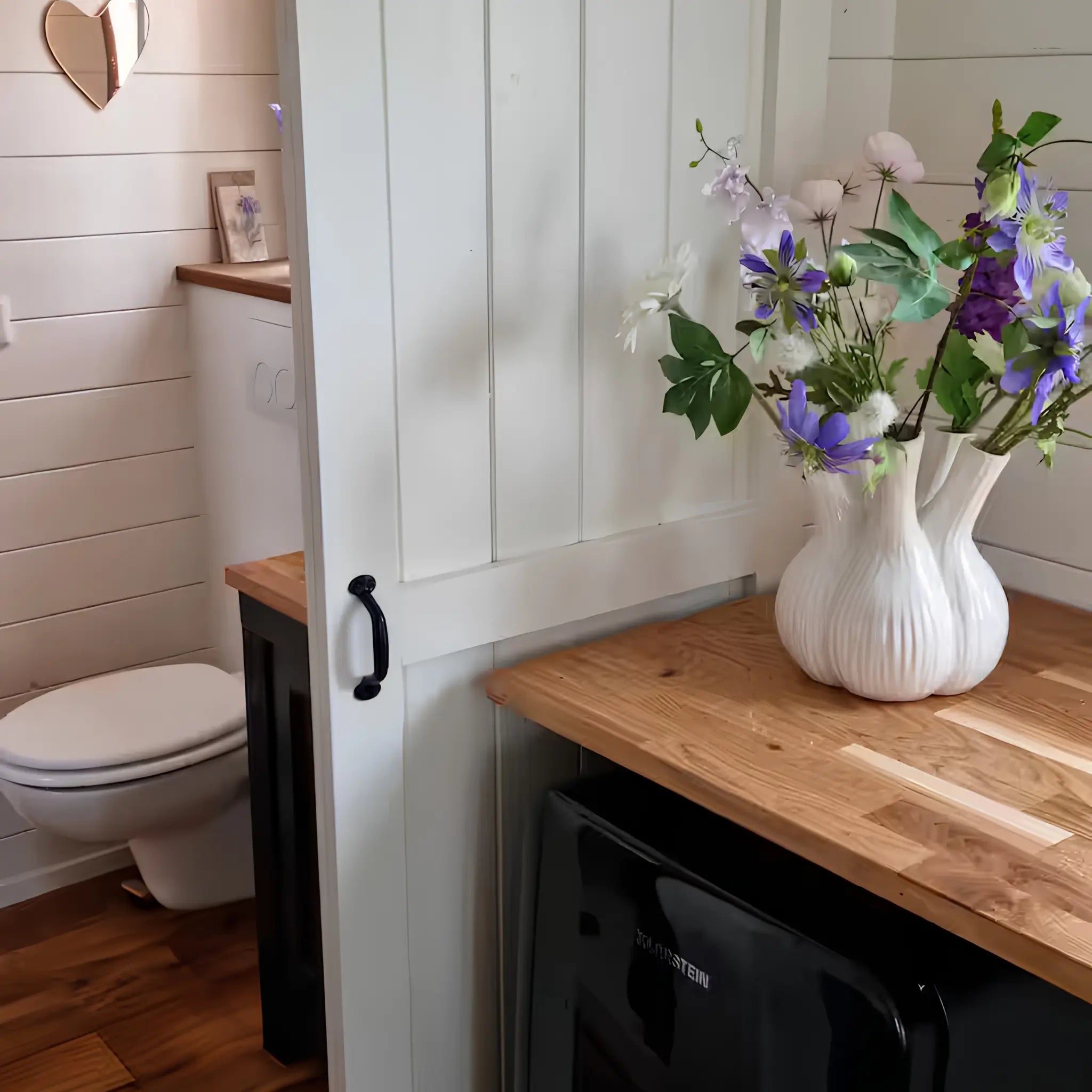 Rustic bathroom entrance with sliding barn door, wooden countertops, and floral decor inside a luxury shepherd’s hut.