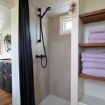 Modern bathroom interior with black rainfall shower, wooden shelving, and neatly folded towels.