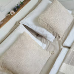 Close-up of cosy double bed with soft neutral bedding, textured cushions, and floral styling.