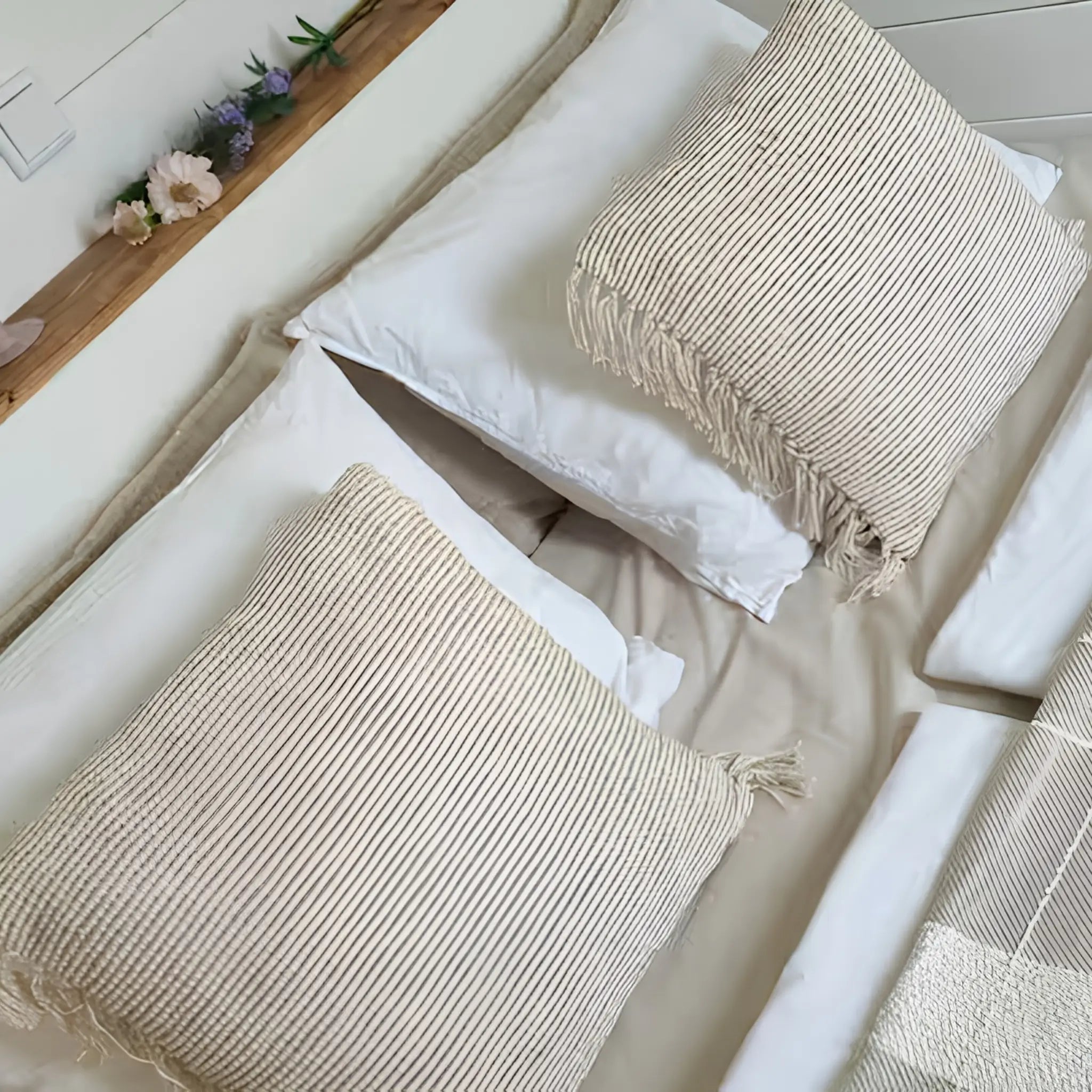 Close-up of cosy double bed with soft neutral bedding, textured cushions, and floral styling.