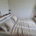 Minimalist bedroom interior with double bed, white panelled walls, soft neutral bedding, and warm wooden accents.