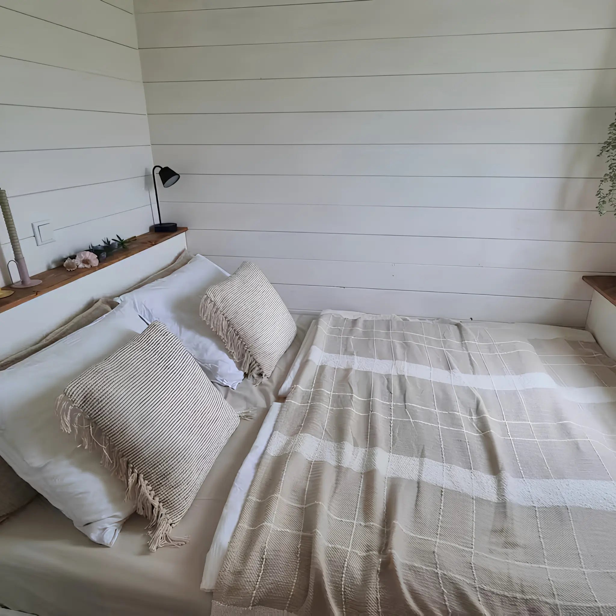 Minimalist bedroom interior with double bed, white panelled walls, soft neutral bedding, and warm wooden accents.