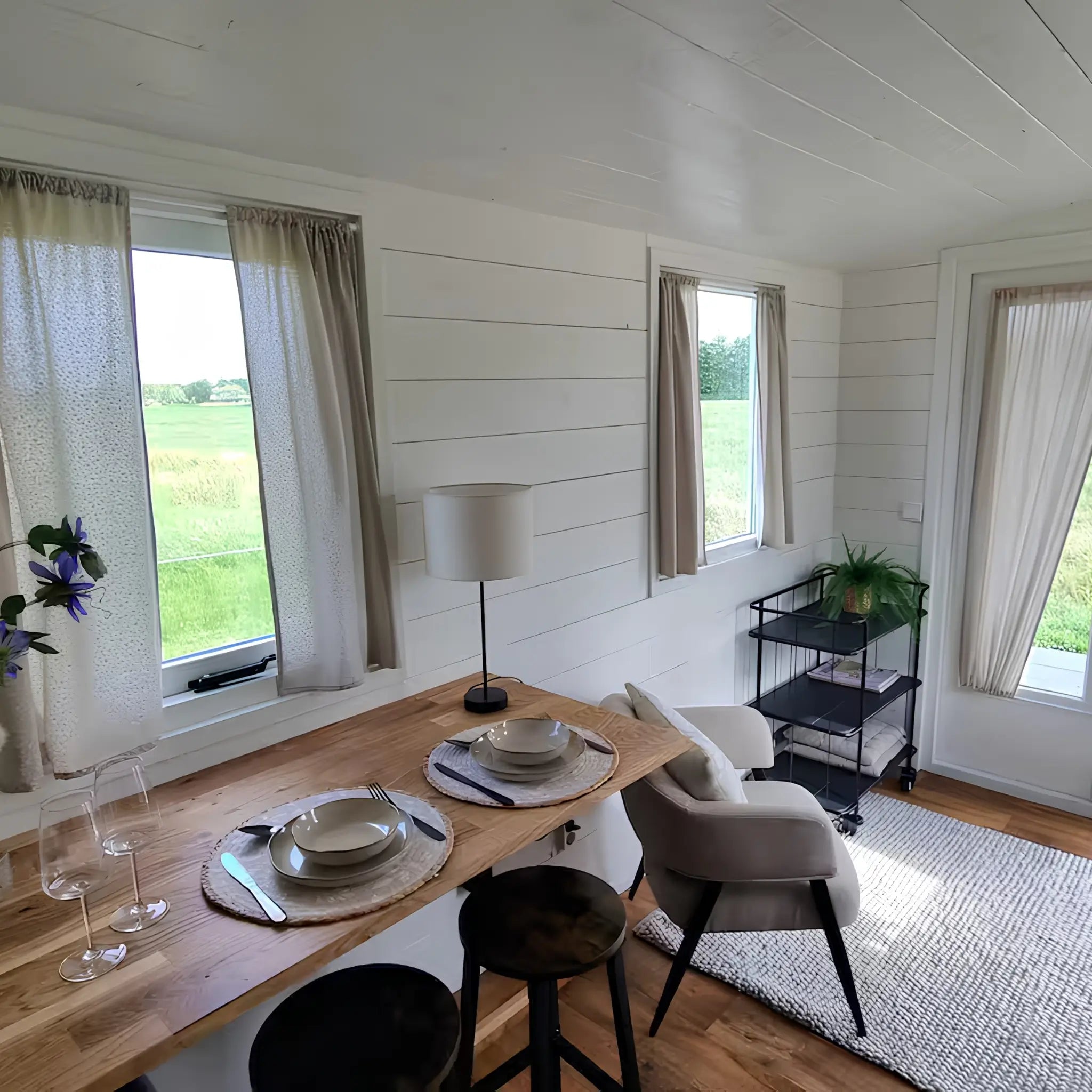 Bright open-plan living and dining area with wooden breakfast bar, armchairs, large windows, and countryside views.