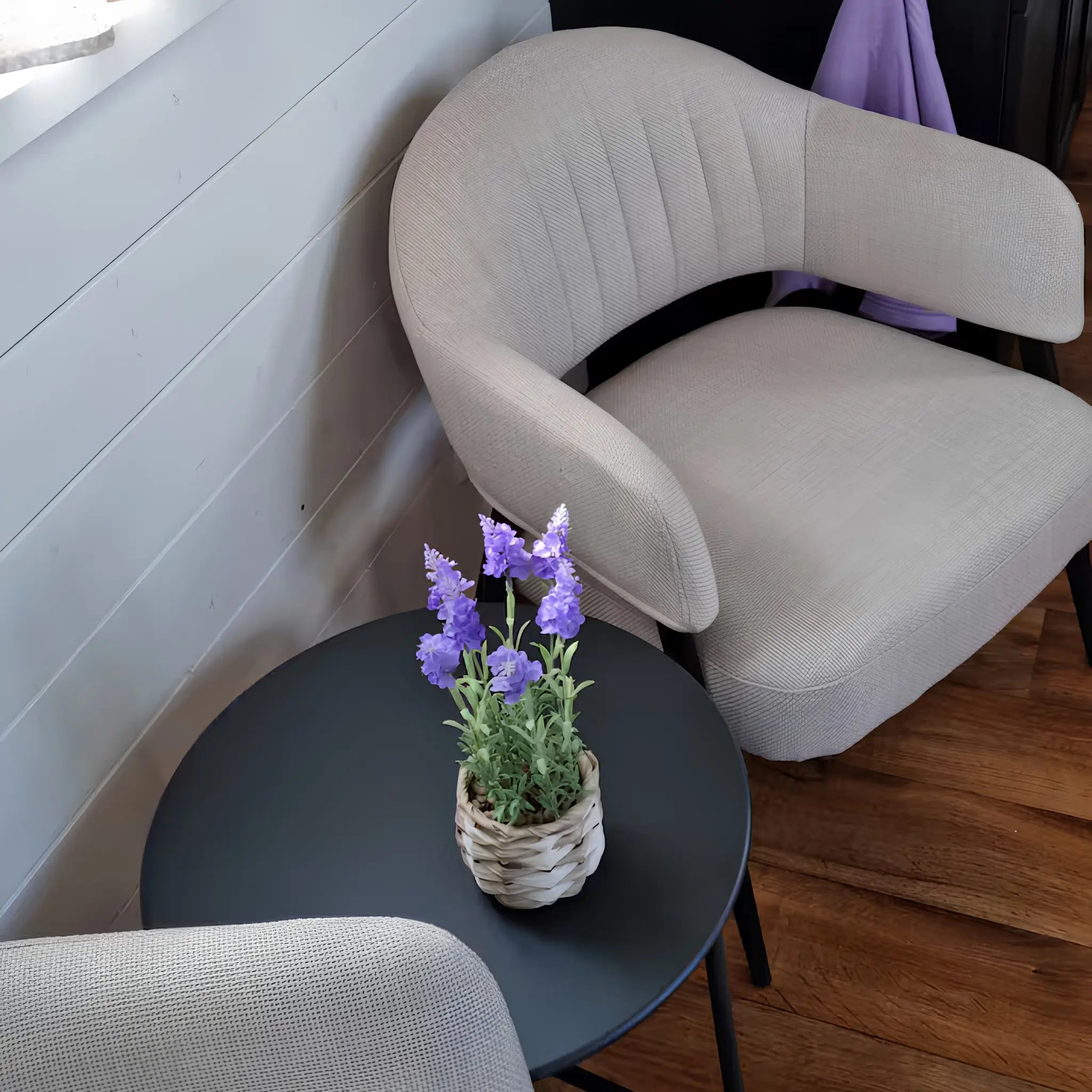 Cosy seating area with soft upholstered armchairs, black side table, and small lavender plant decoration.