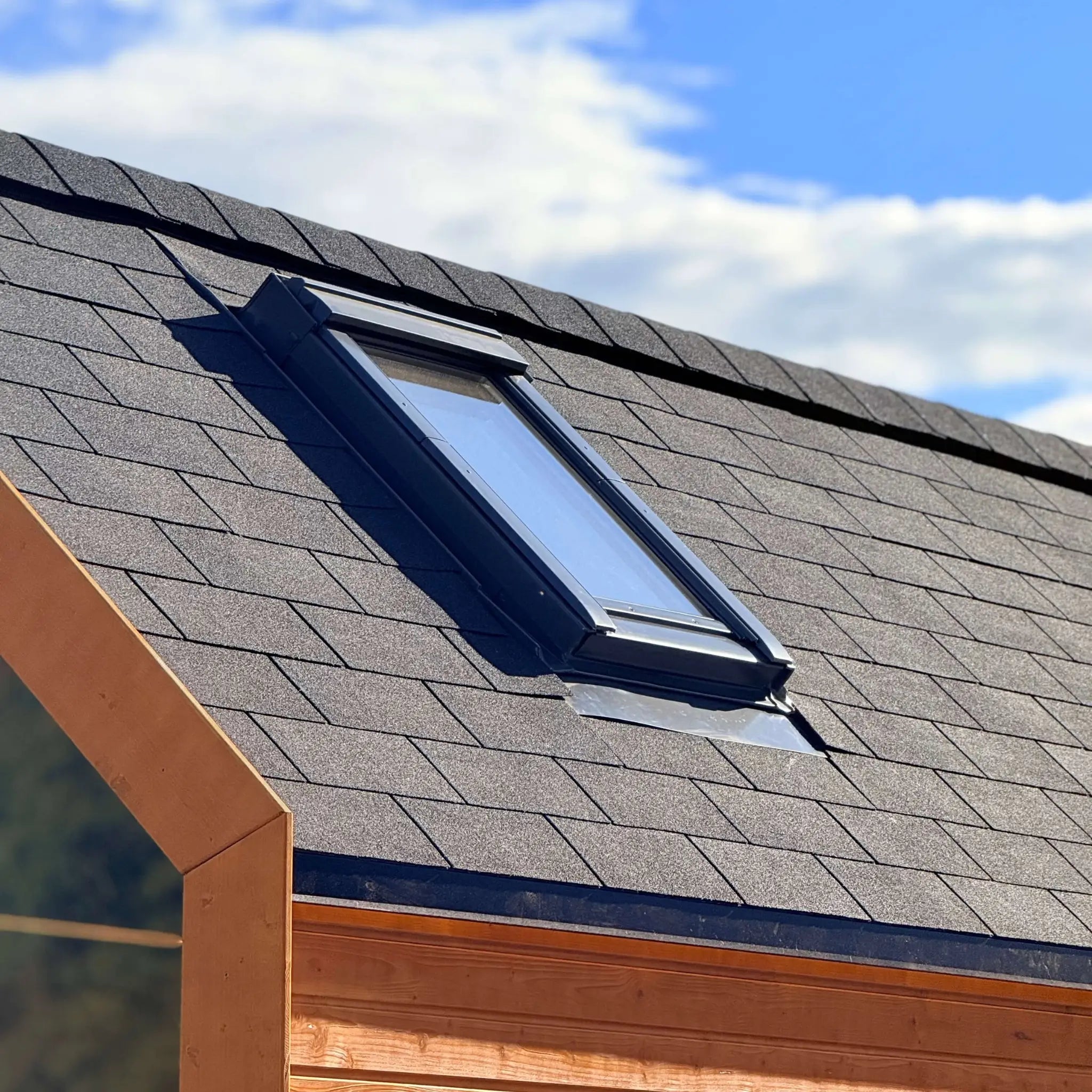 Close-up of insulated skylight roof window on luxury glamping pod with modern shingle roofing and timber exterior finish.